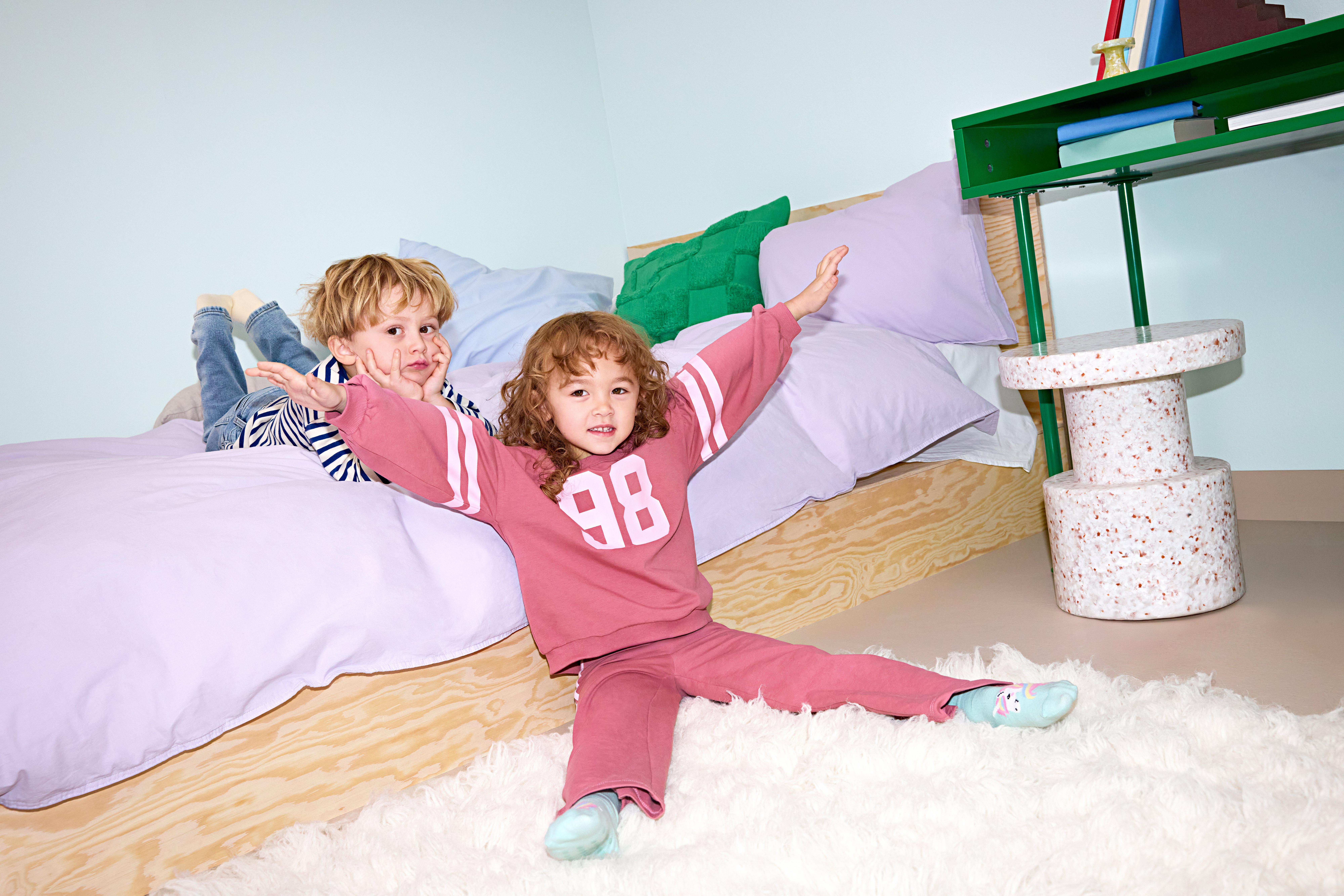 Two kids, a boy and a girl, in colorful clothes against a sofa.