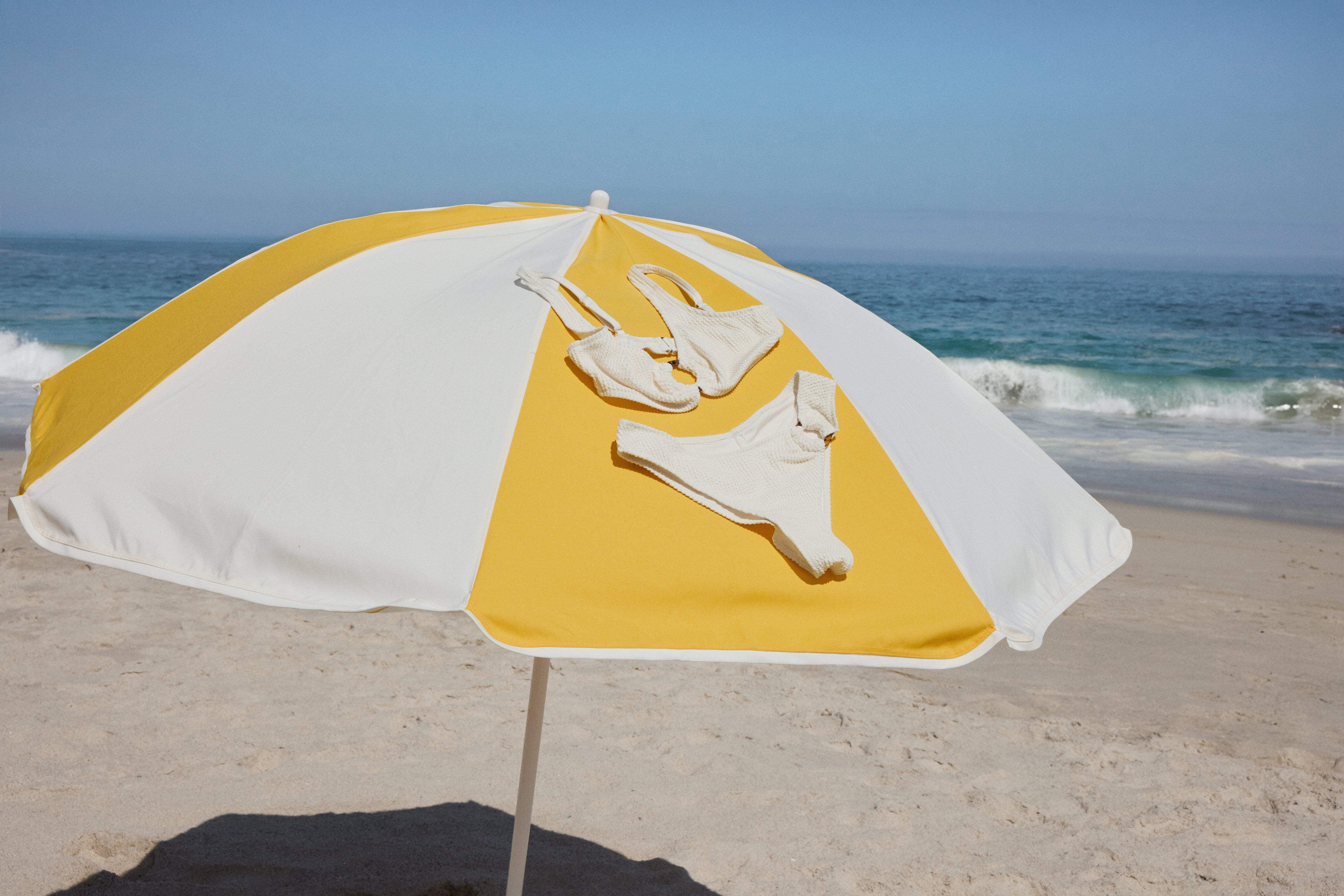 A light yellow bikini is drying on a yellow and white striped parasol.
