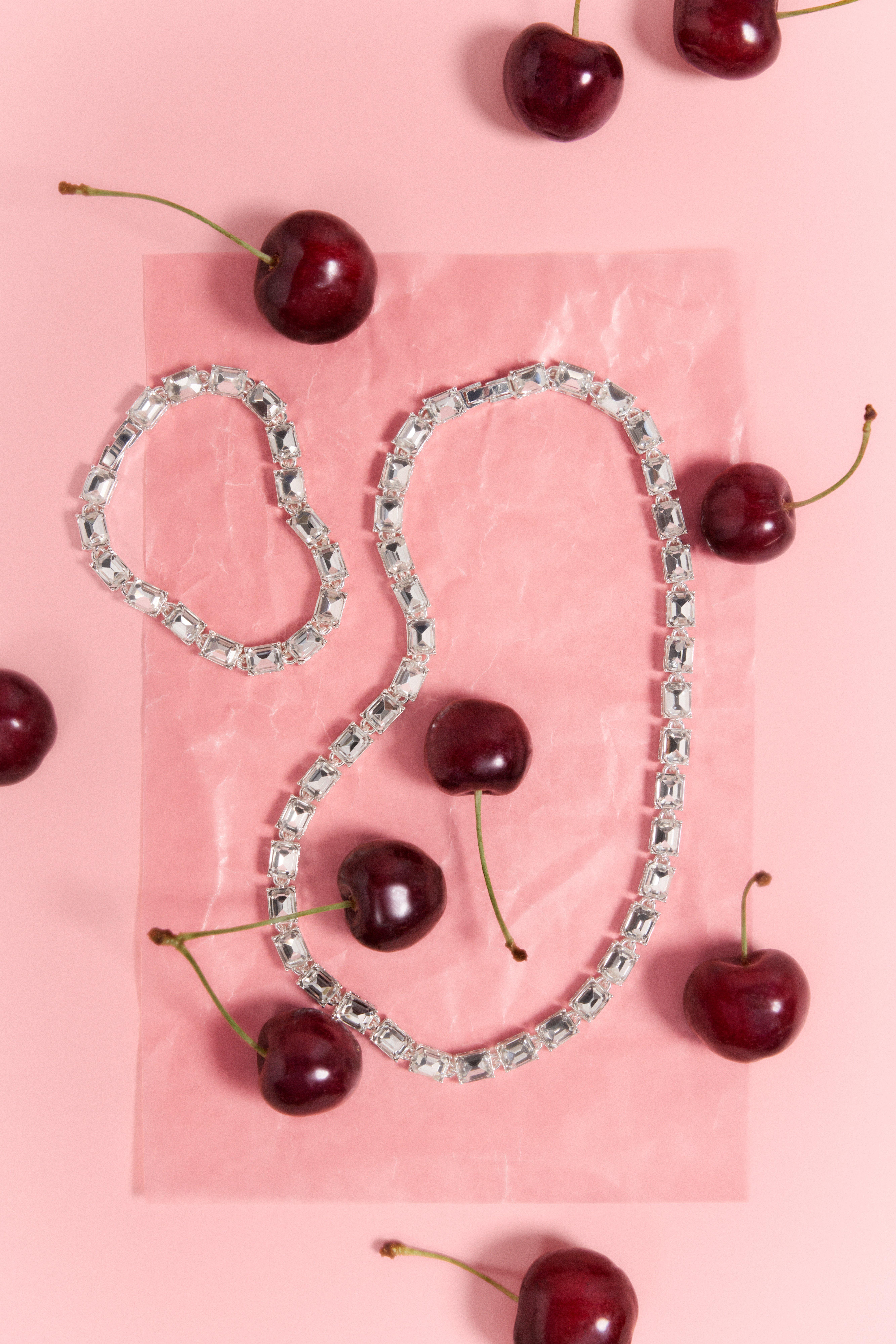 Detailní záběr stříbrného náhrdelníku a náramku ležících na růžovém pozadí.