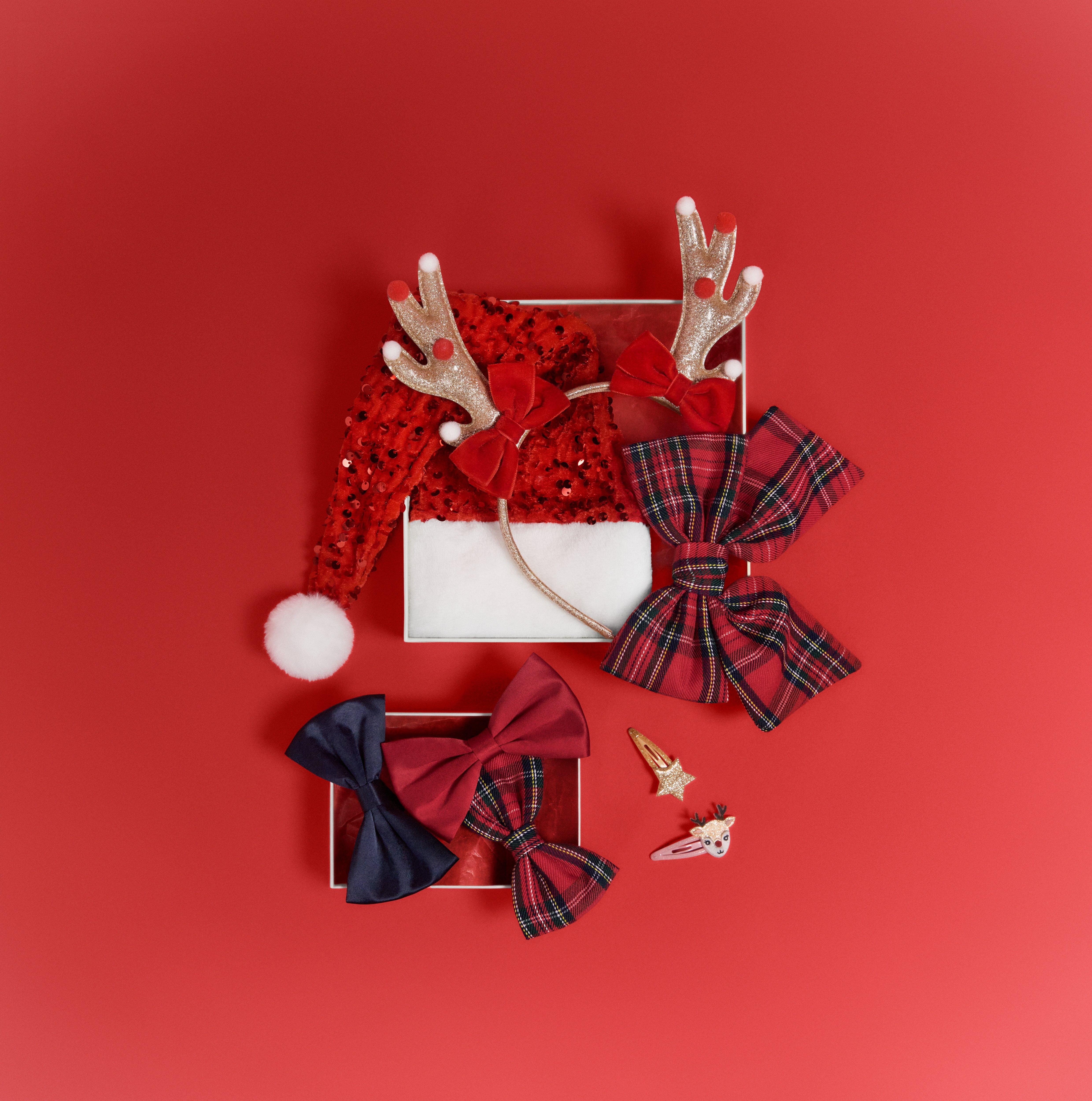 Několik různých vánočních doplňků, jako jsou sponky do vlasů, paroží soba, mašle a další, leží na červeném povrchu.
