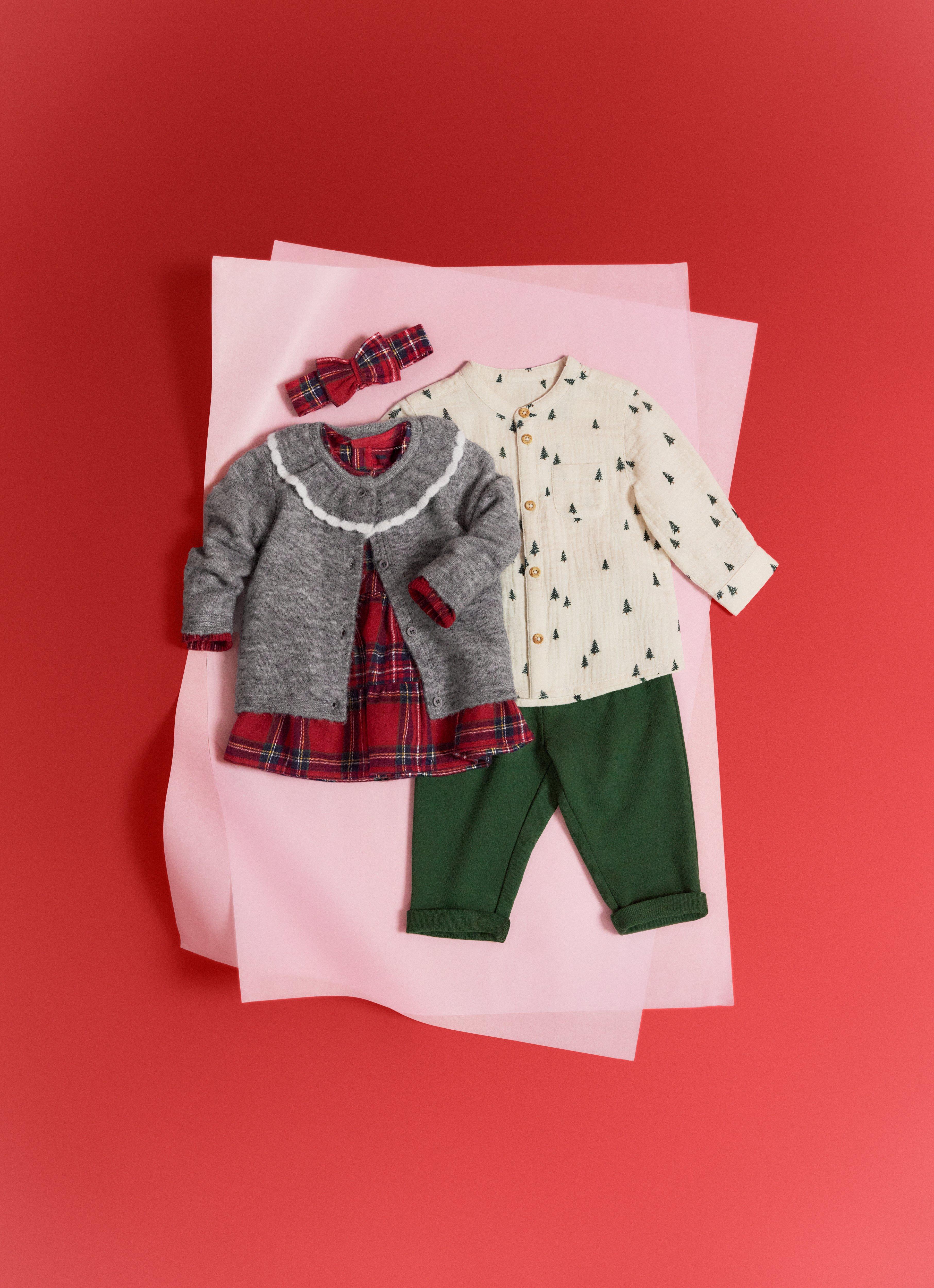 Detailní záběr několika věcí pro miminka ležících na červeném balicím papíře.