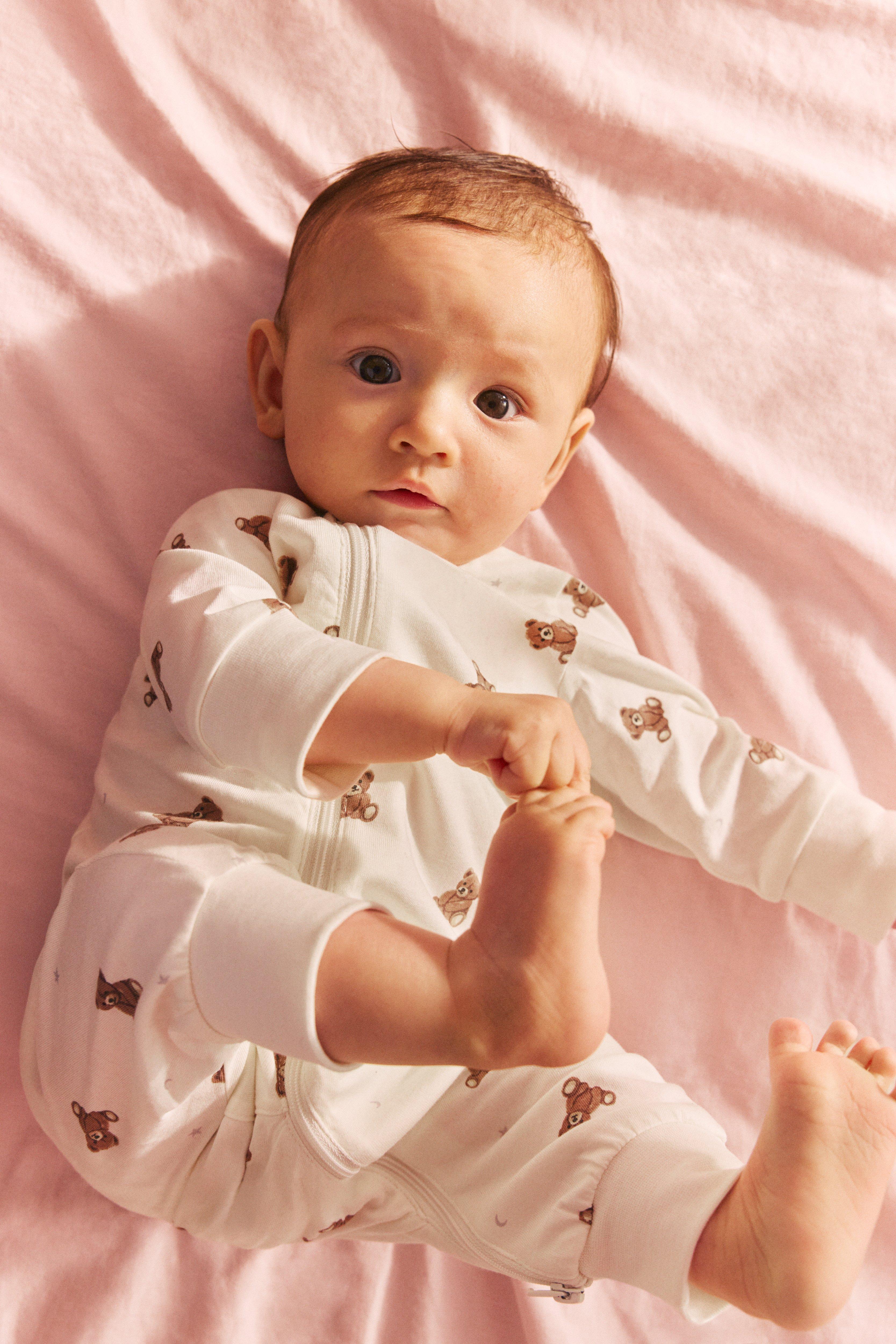 A happy and laughing baby in yellow summer clothes stands in a meadow full of flowers.