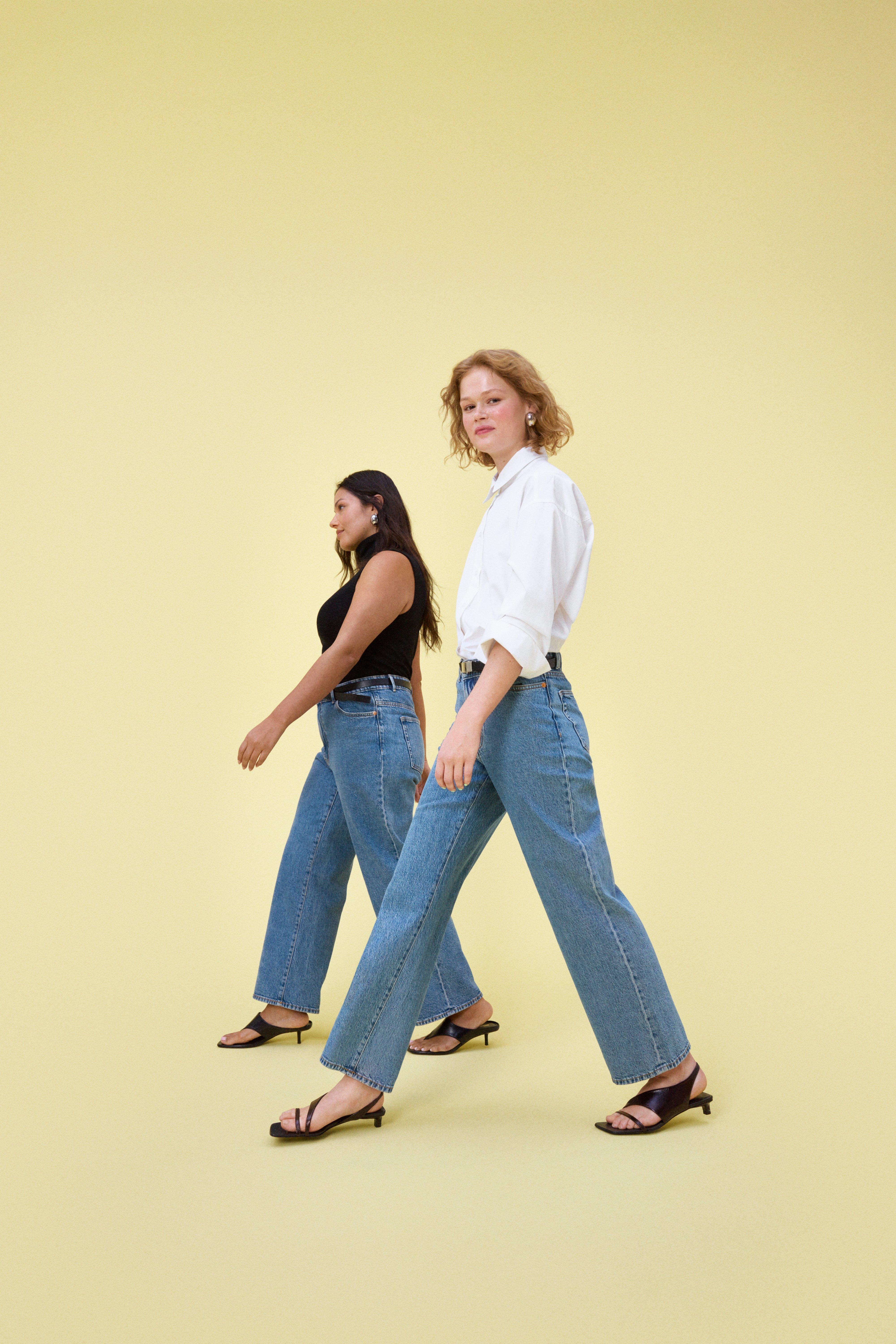 Two women dressed in jeans walk past the camera.