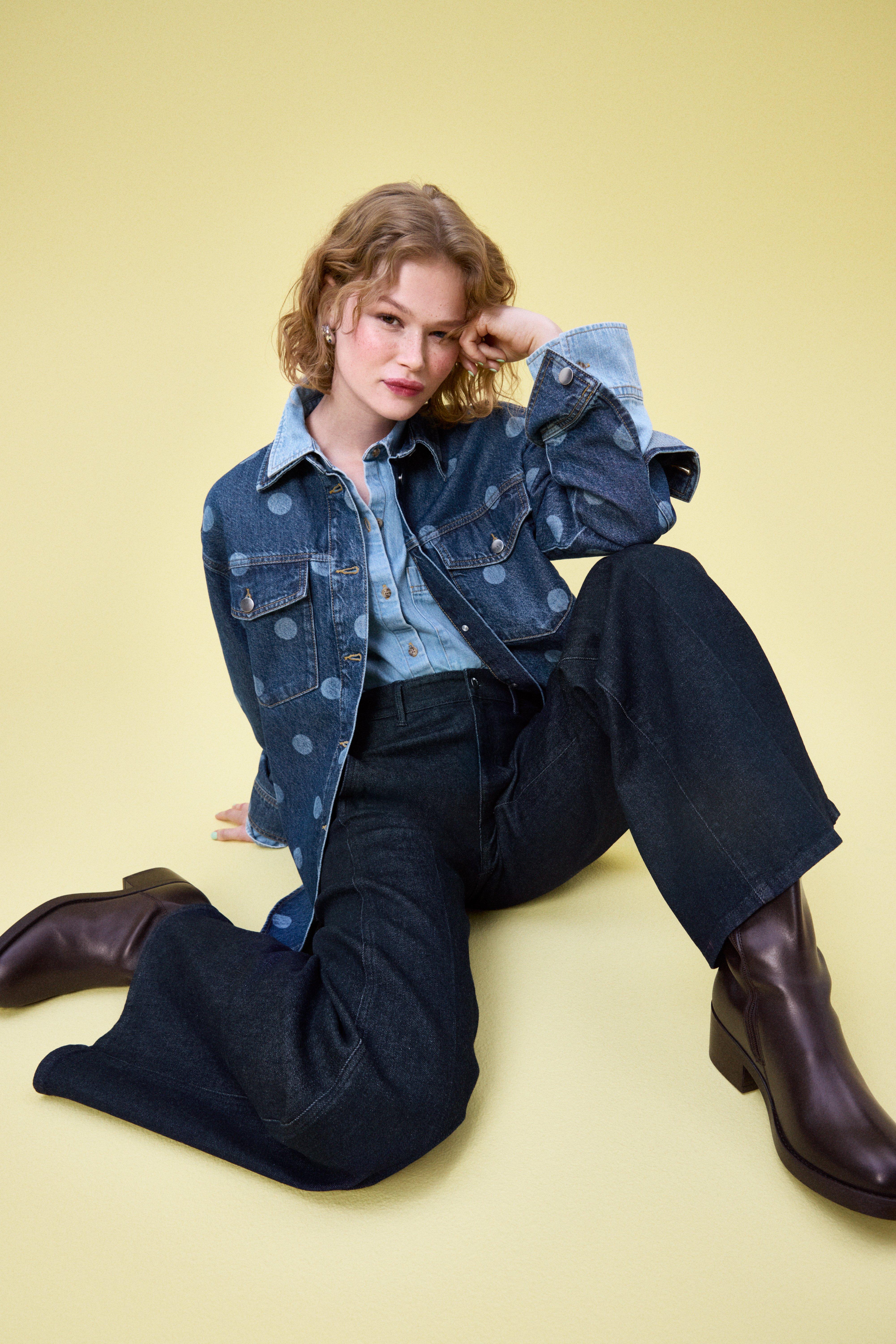 A woman wearing a dark blue denim jackt with dots, a light blue denim shirt and a pair of dark blue jeans.