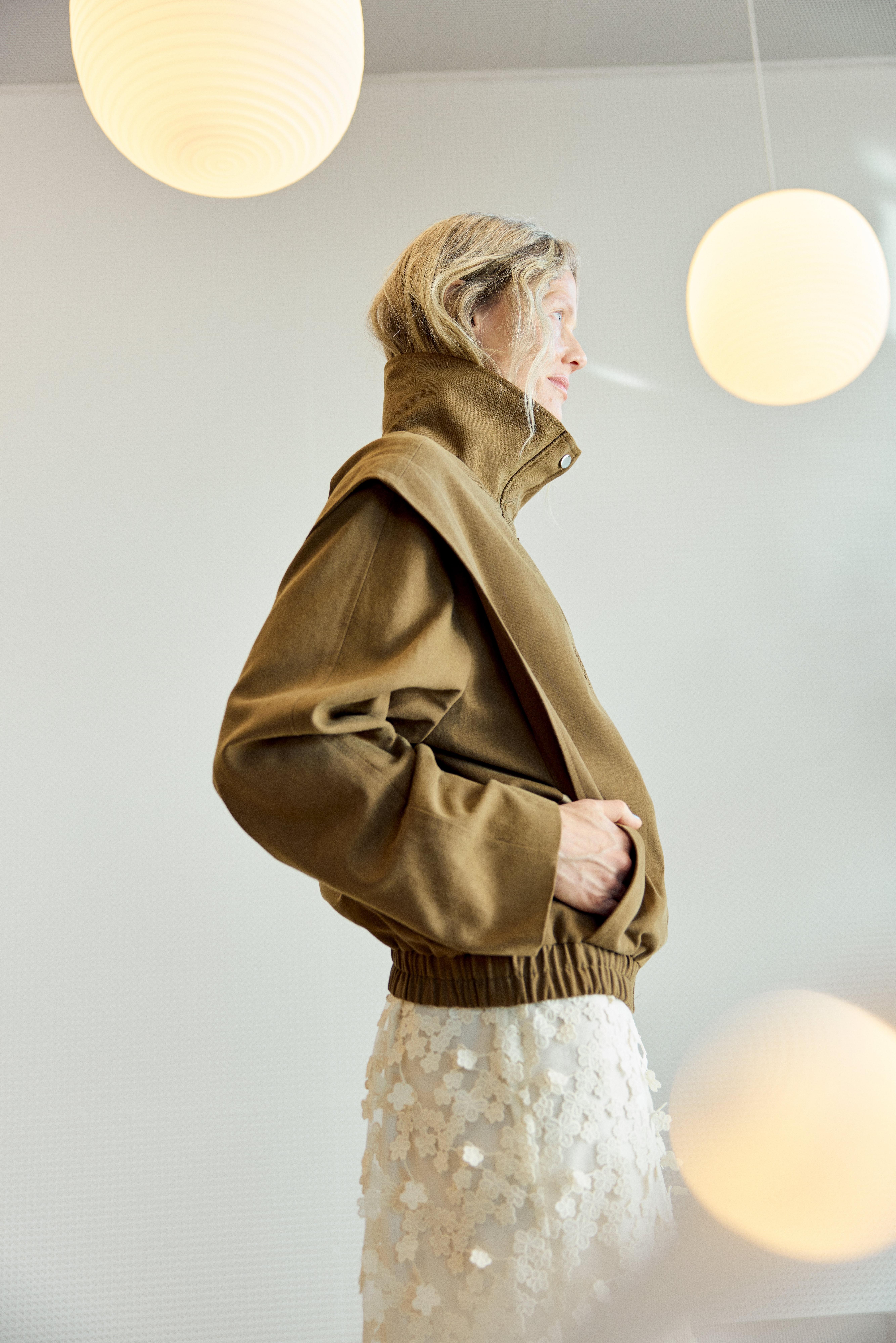 Picture taken from the side of a woman in a light brown jacket with a high collar.