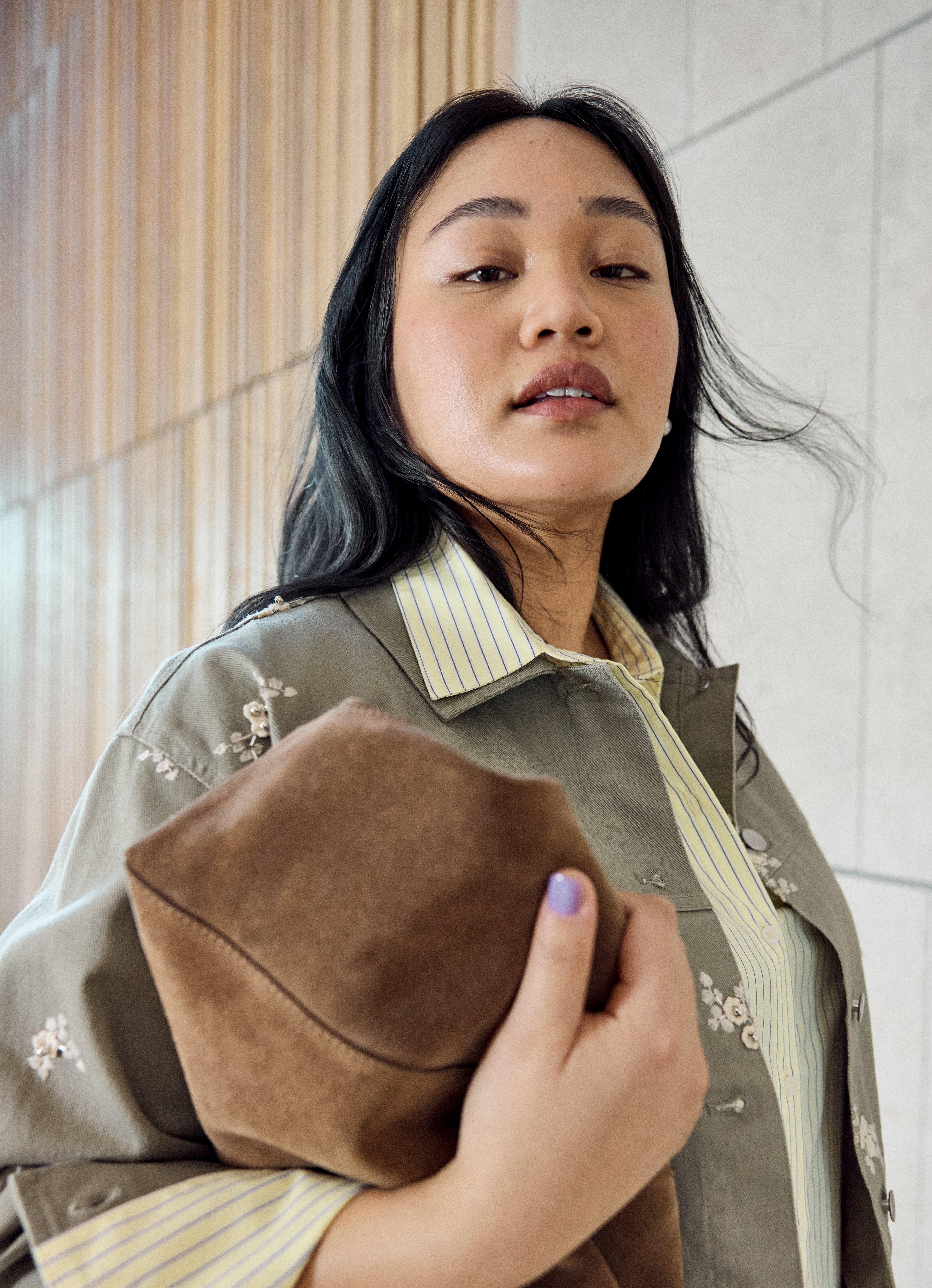  Close-up of a woman wearing a khaki jacket with embroidered flowers.