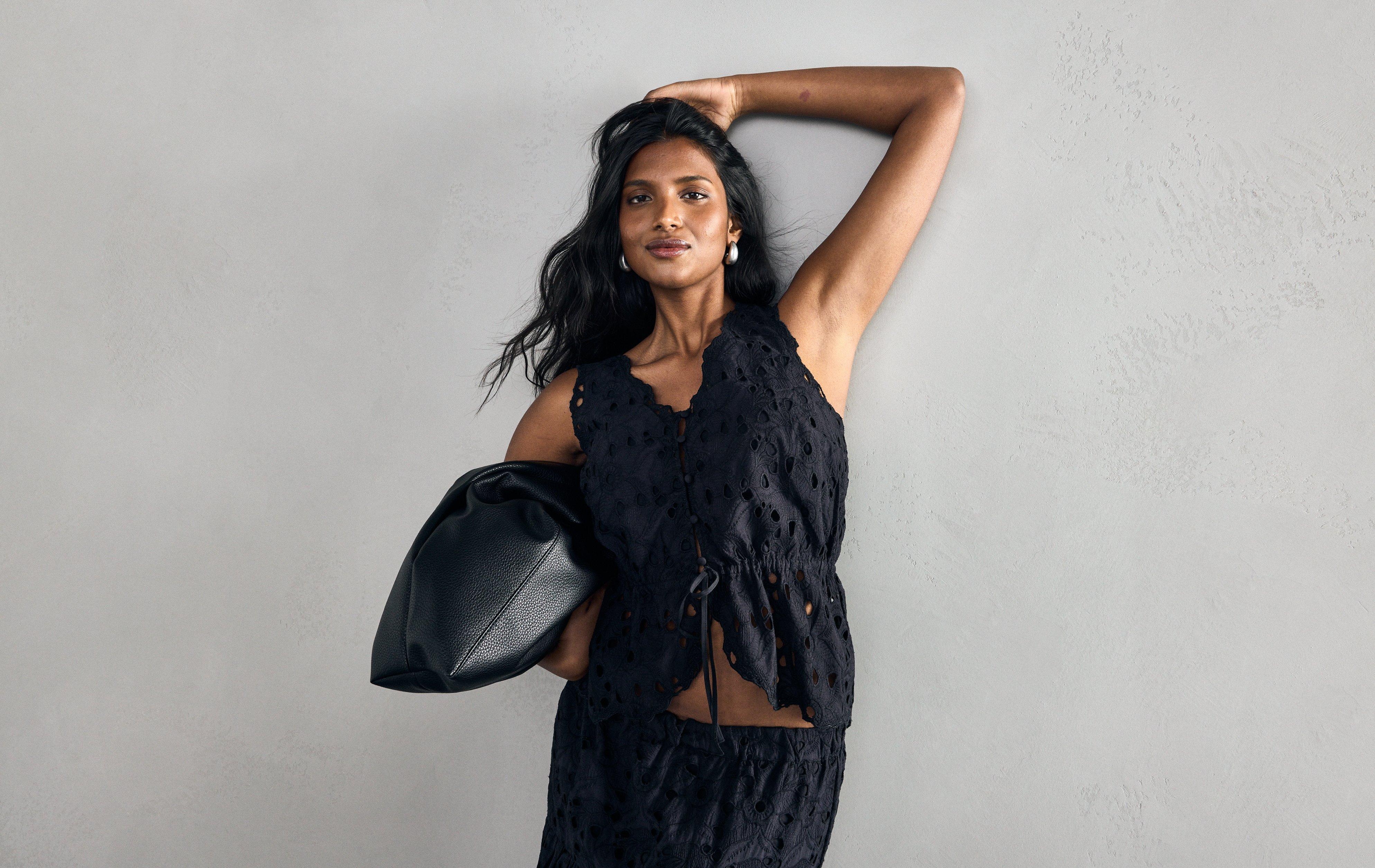  Close-up of a woman wearing a black sleeveless top with broderie anglaise and button closure at the front.