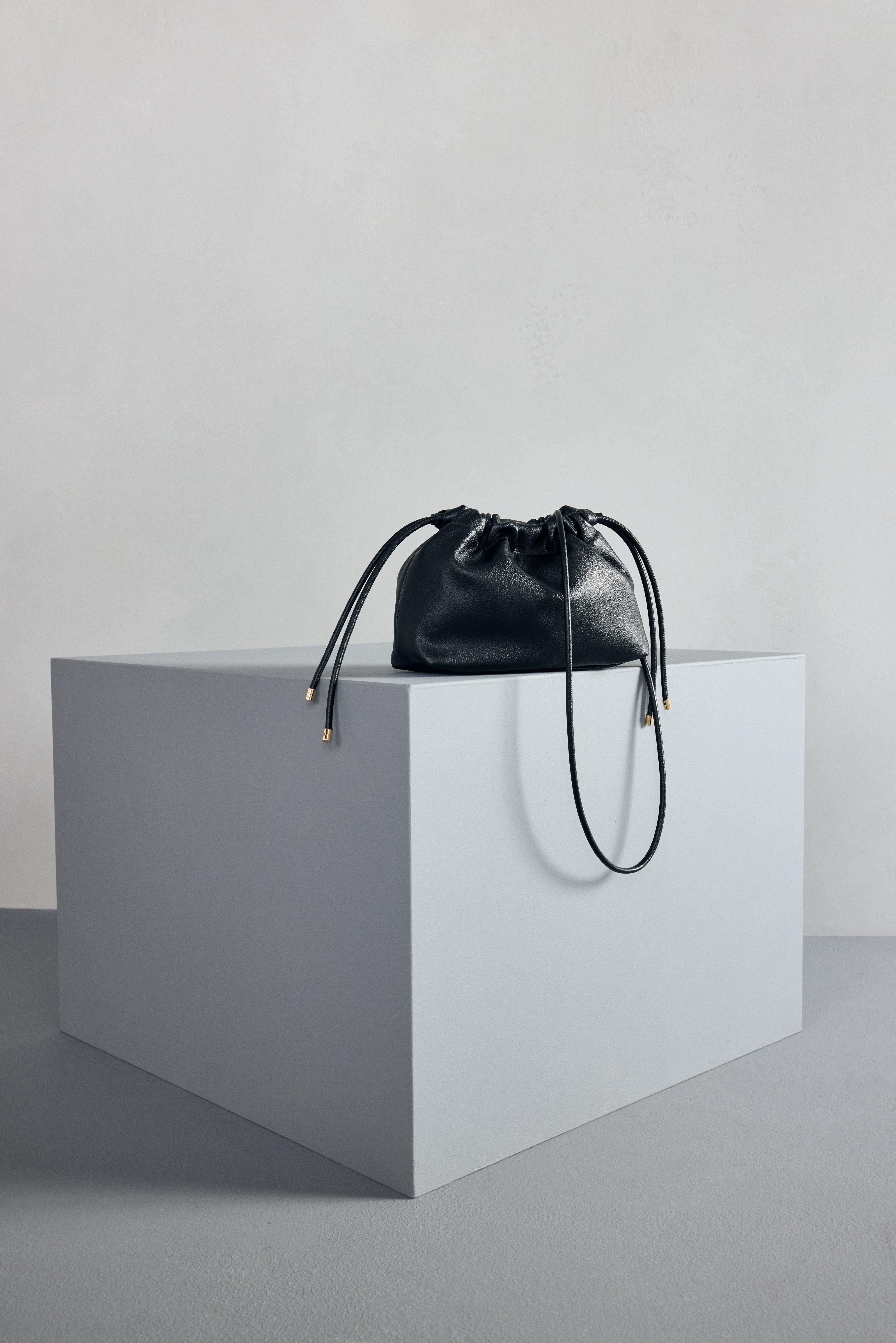A stylish, black shoulder bag in imitation leather stranding on a table.