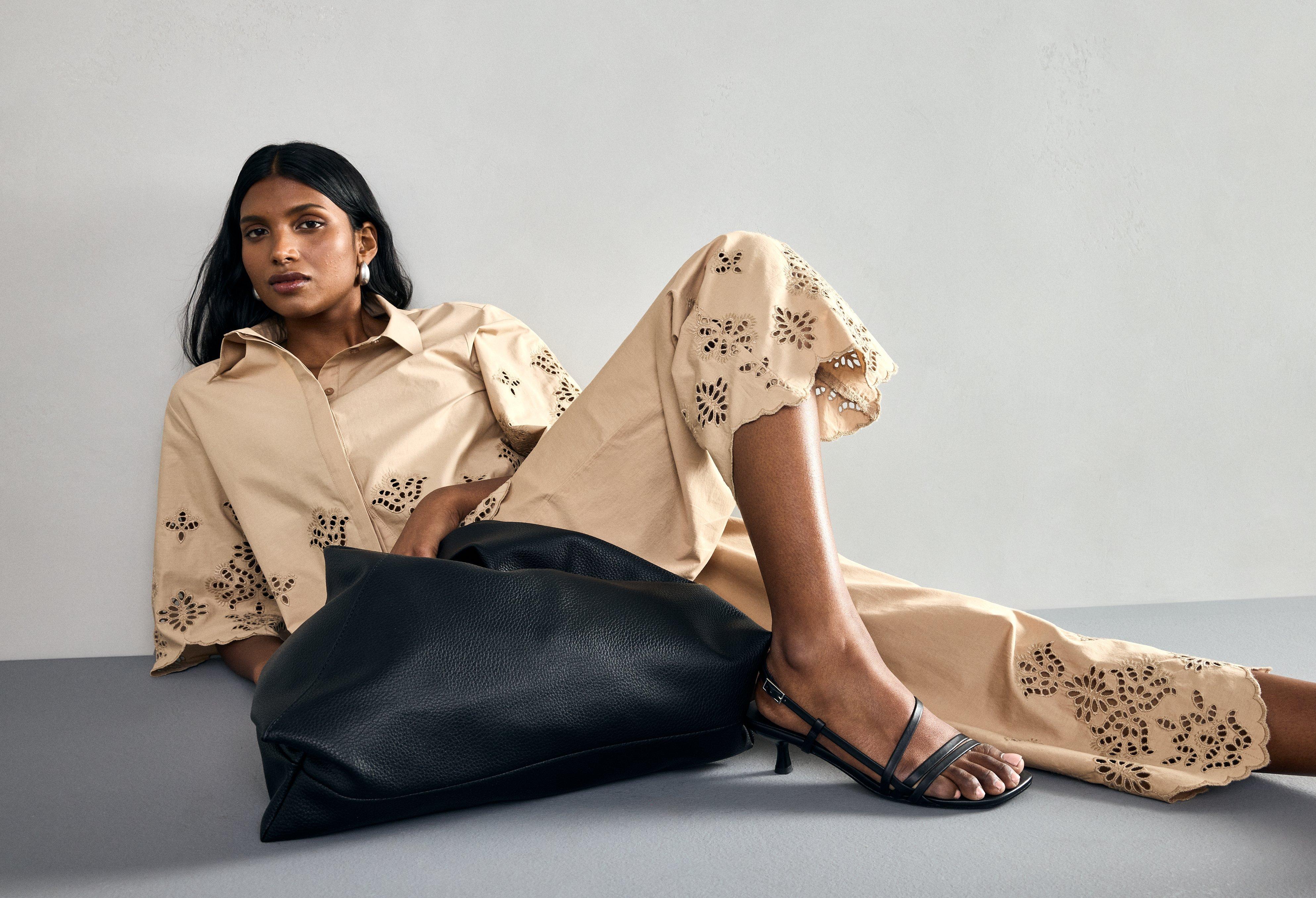  A woman wearing a beige top and cropped pants, both woven cotton and with embroidered details. The woman is holding a large black bag.