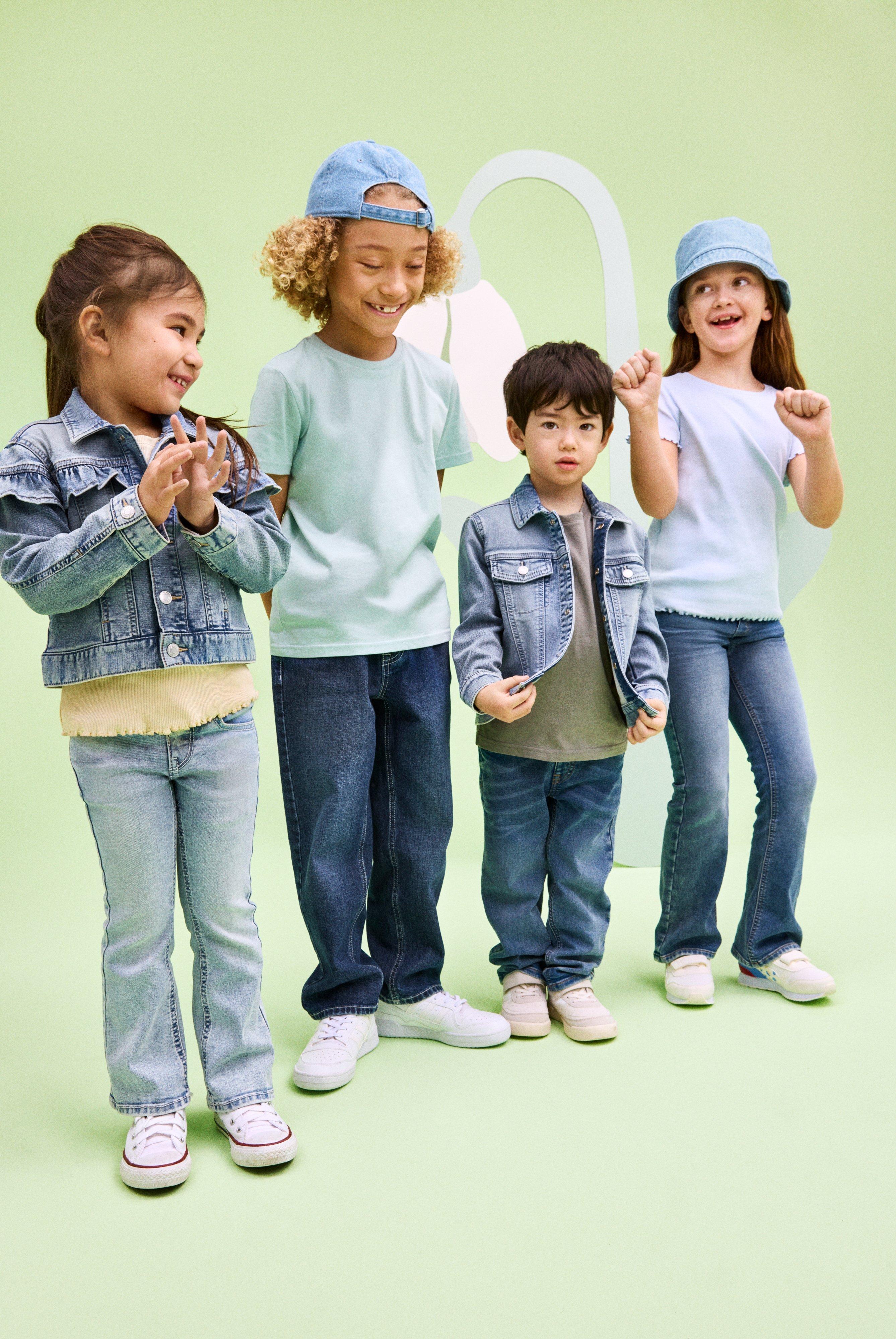 The legs of four kids of different size and age dressed in jeans.