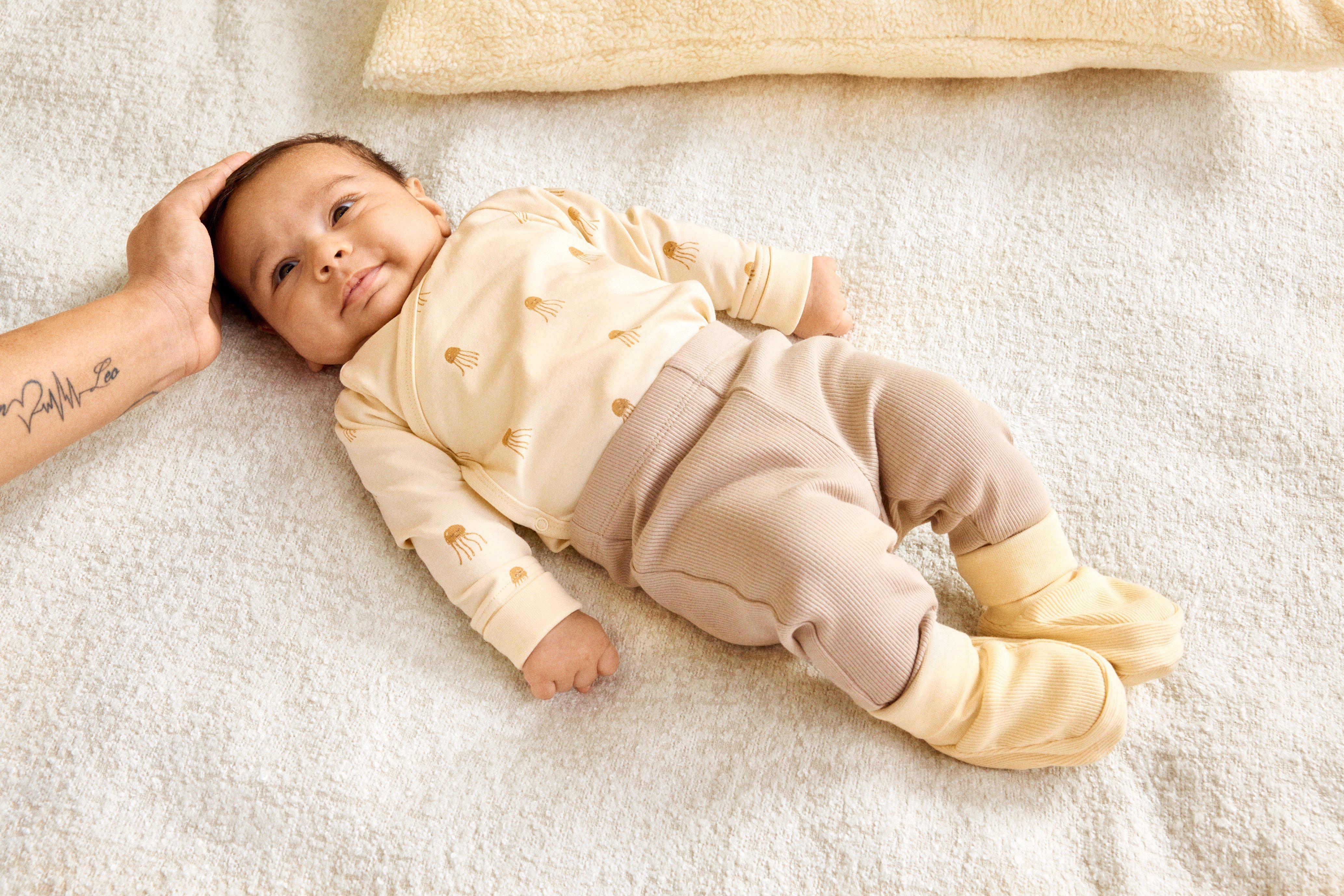 A baby lying on a brown cushion dressed in a natural colored starter kit from Lindex.