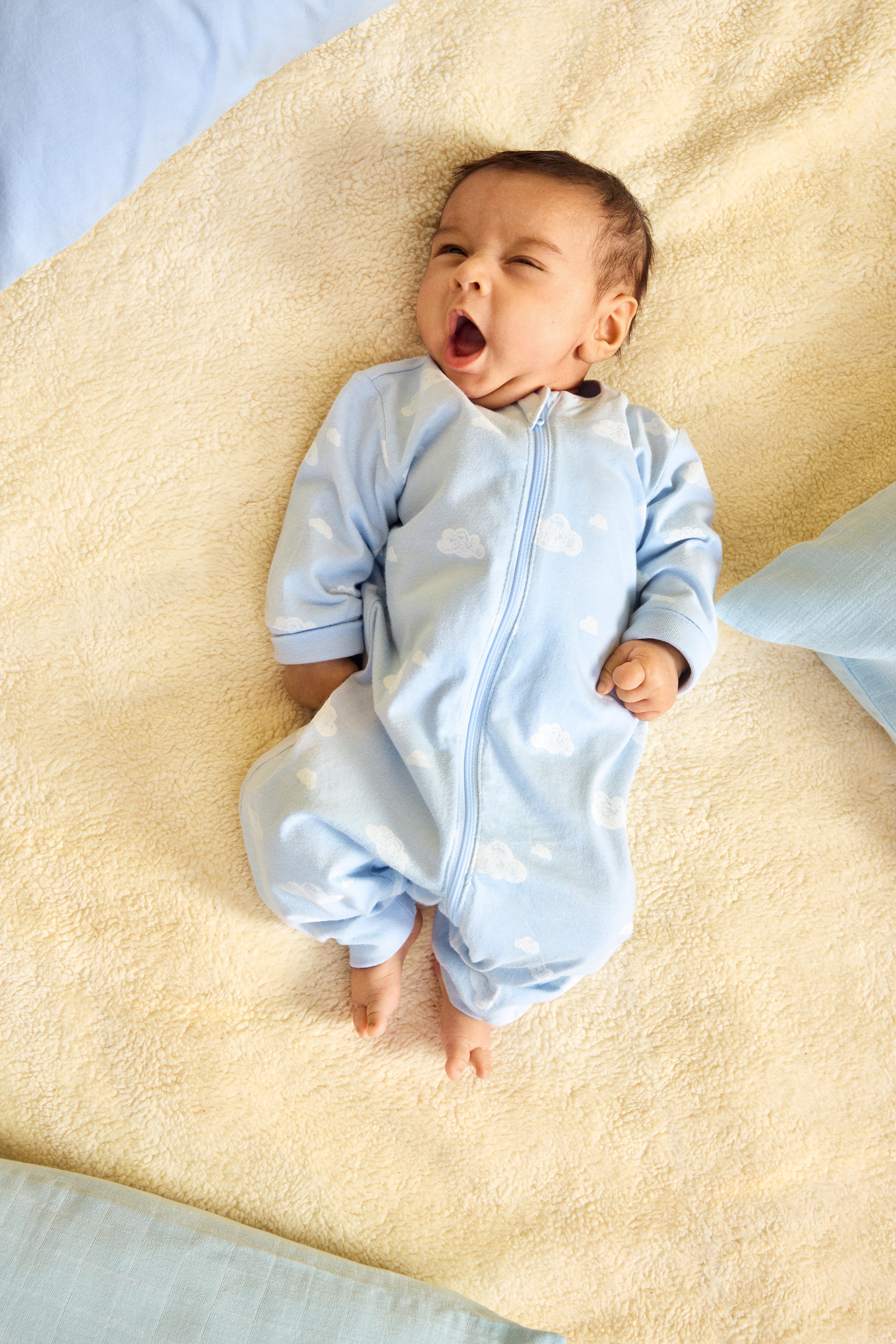  En bebis klädd i blå pyjamas ligger på en blå filt och gäspar stort.
