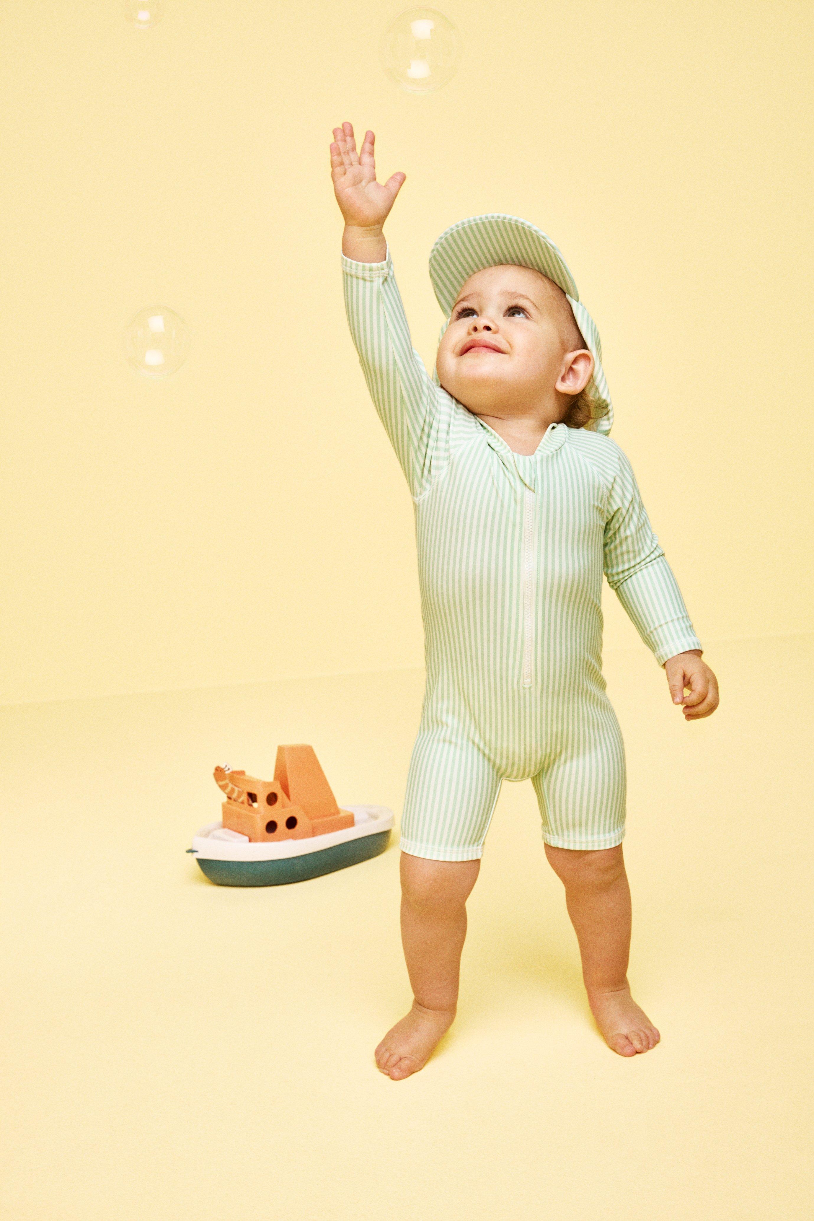 A happy baby in a yellow sun protecting bathing suite running around.