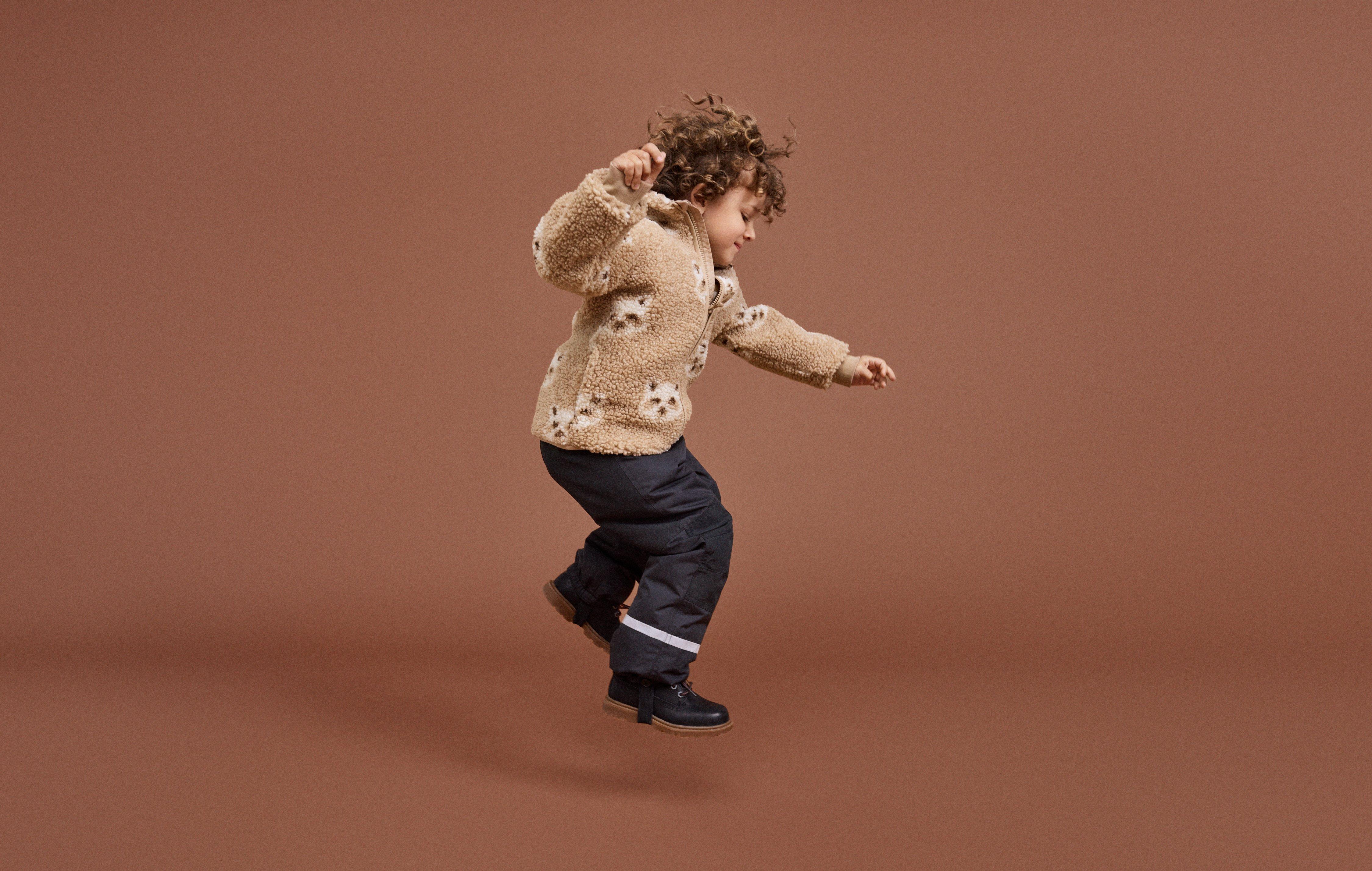 Two children in outerwear from Lindex climbing and playing in a changing room.