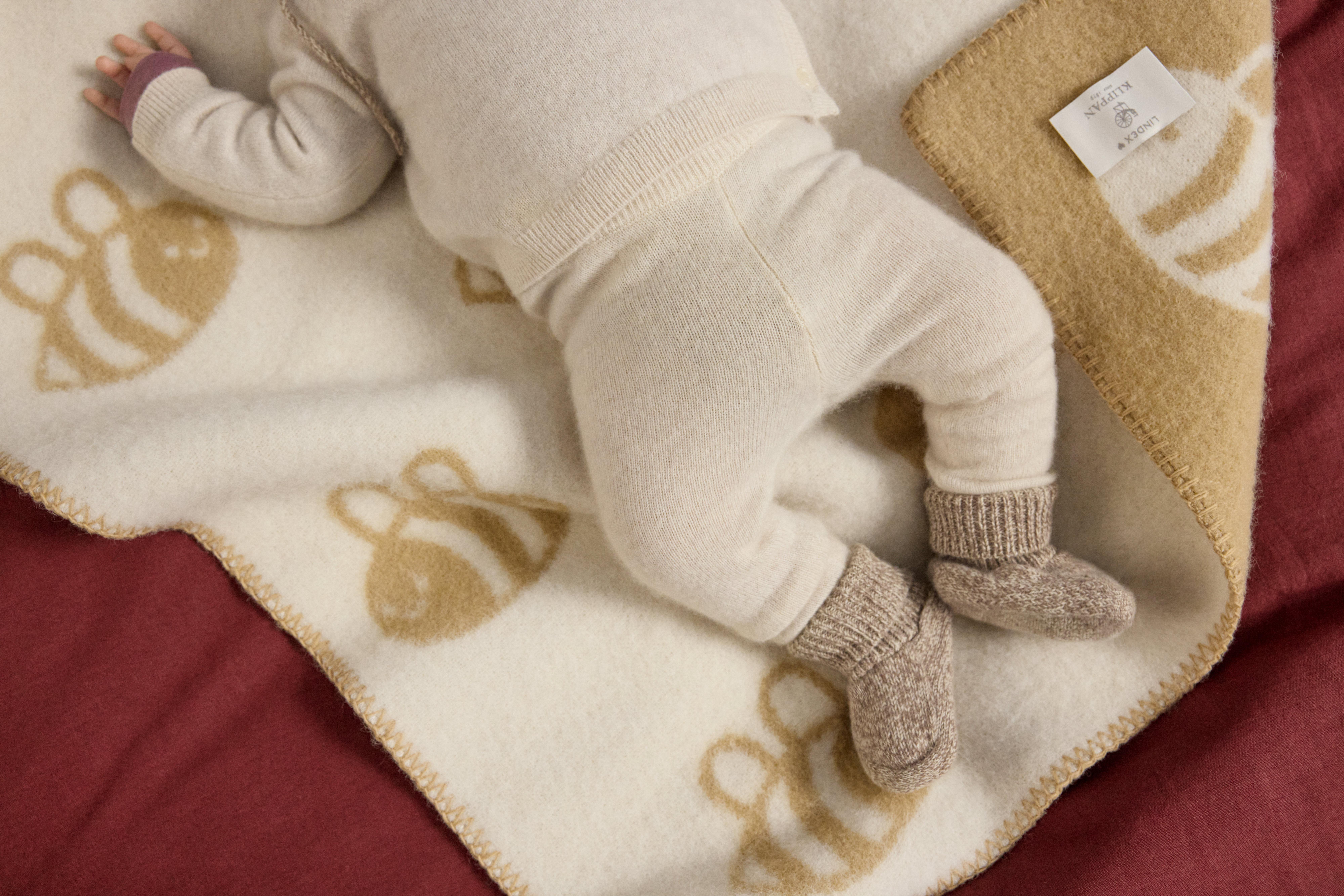  Close-up of a pair of baby legs. The baby is lying on a light beige blanket with a print of bees.