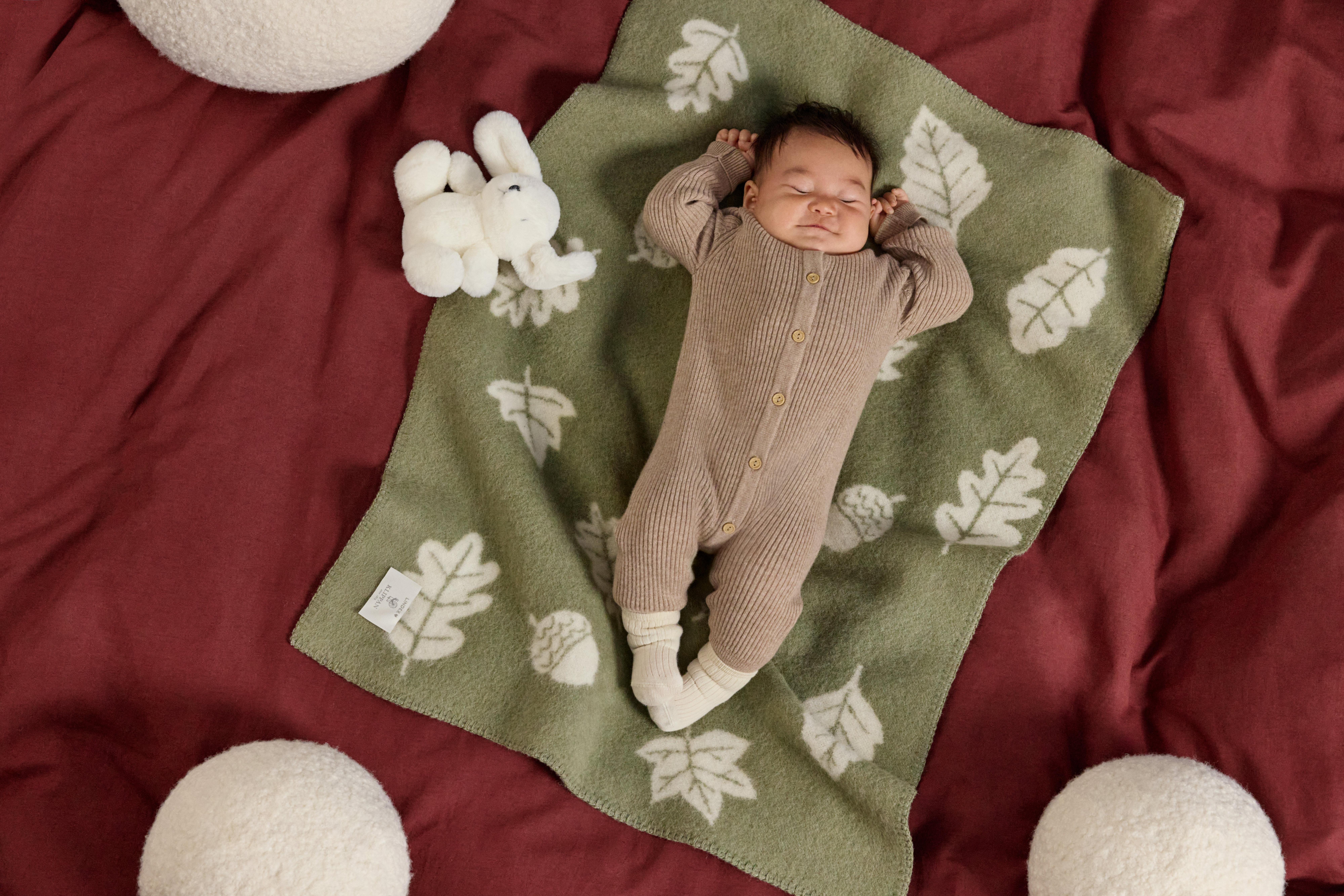 A sleeping baby lies on a green blanket that has a print of leaves.