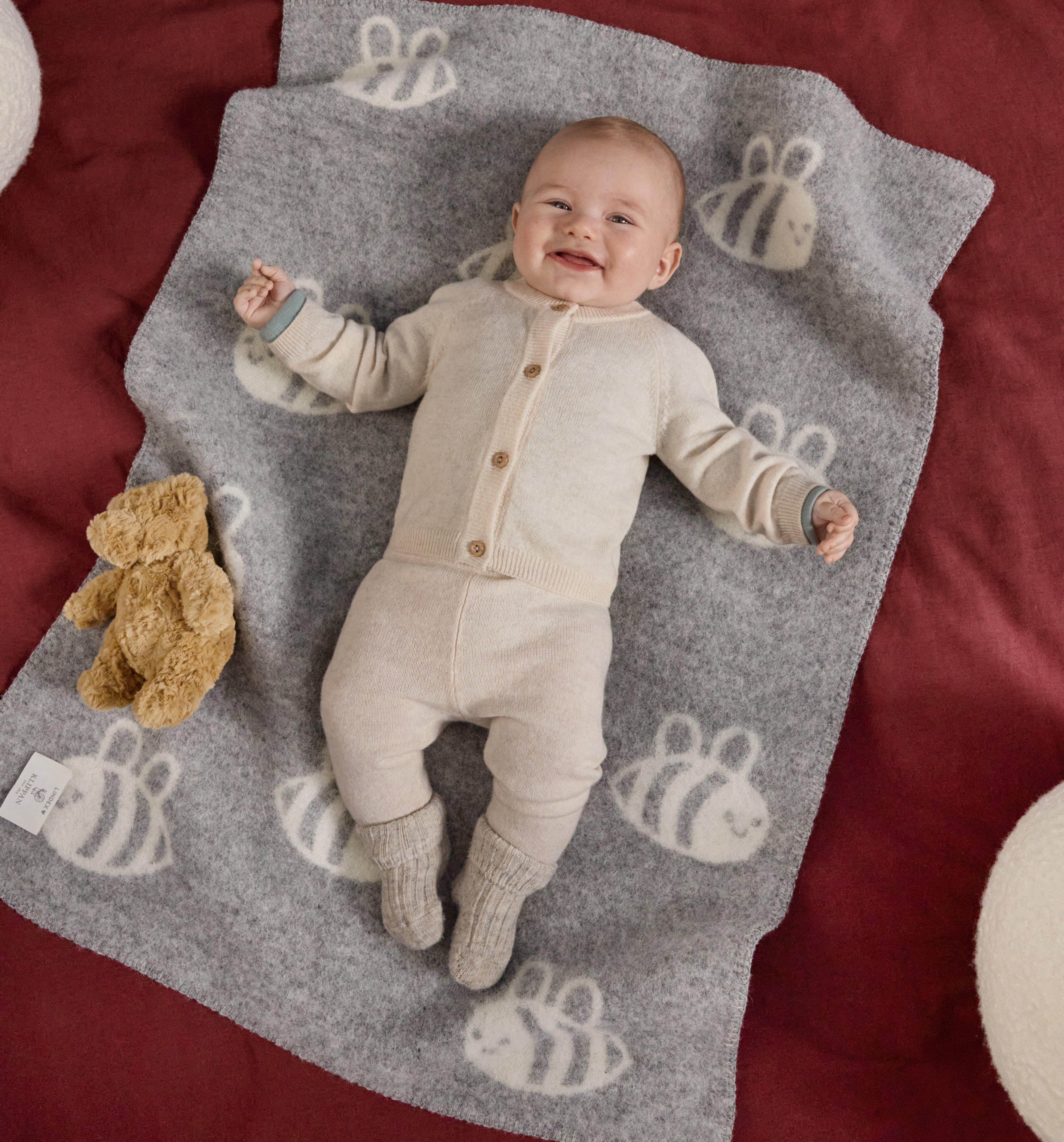 A laughing baby lies on his back on a bright blanket with a print of bees.