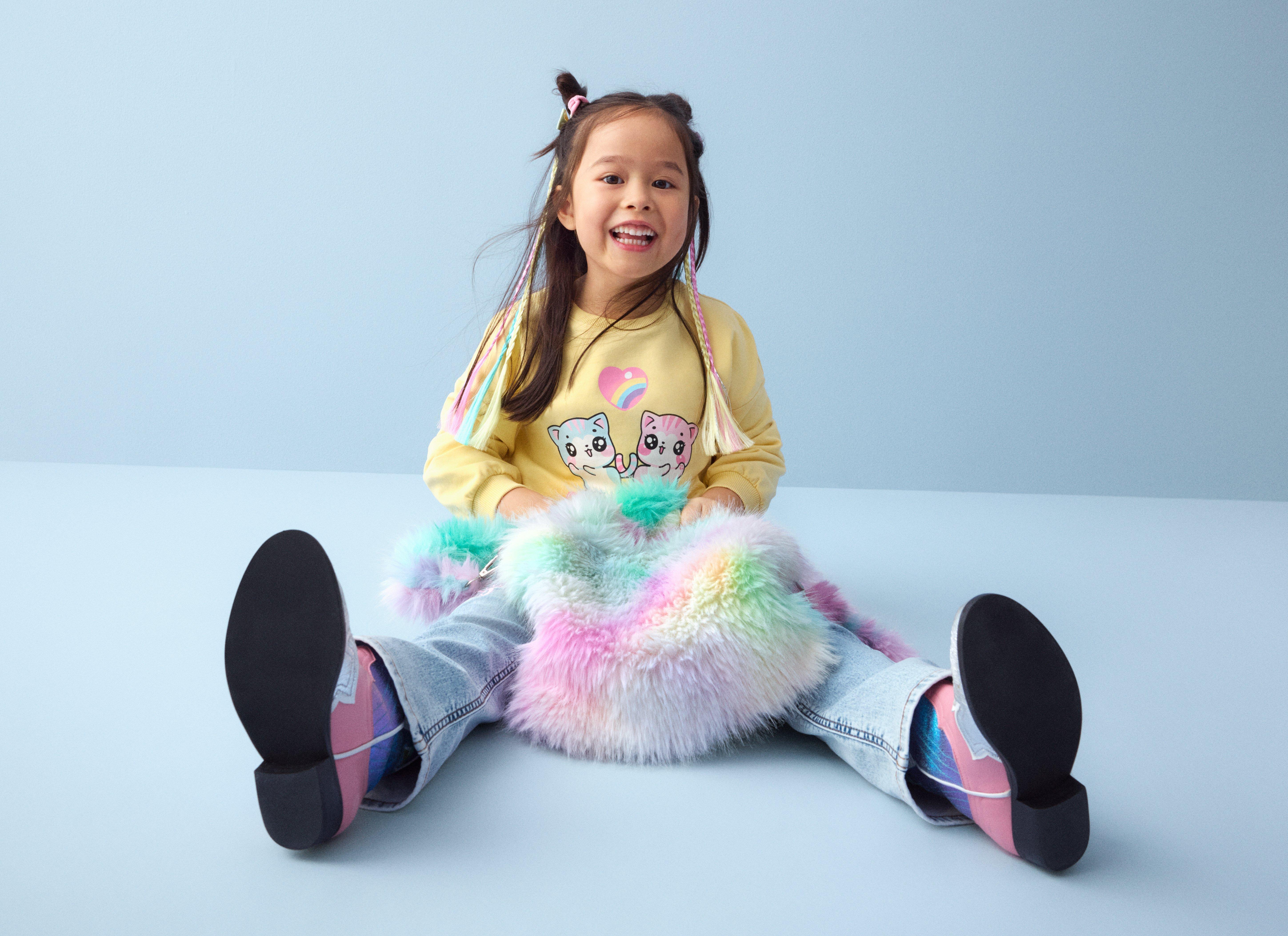 Tyttö, jolla on pörröinen sateenkaarenvärinen laukku, istuu lattialla.