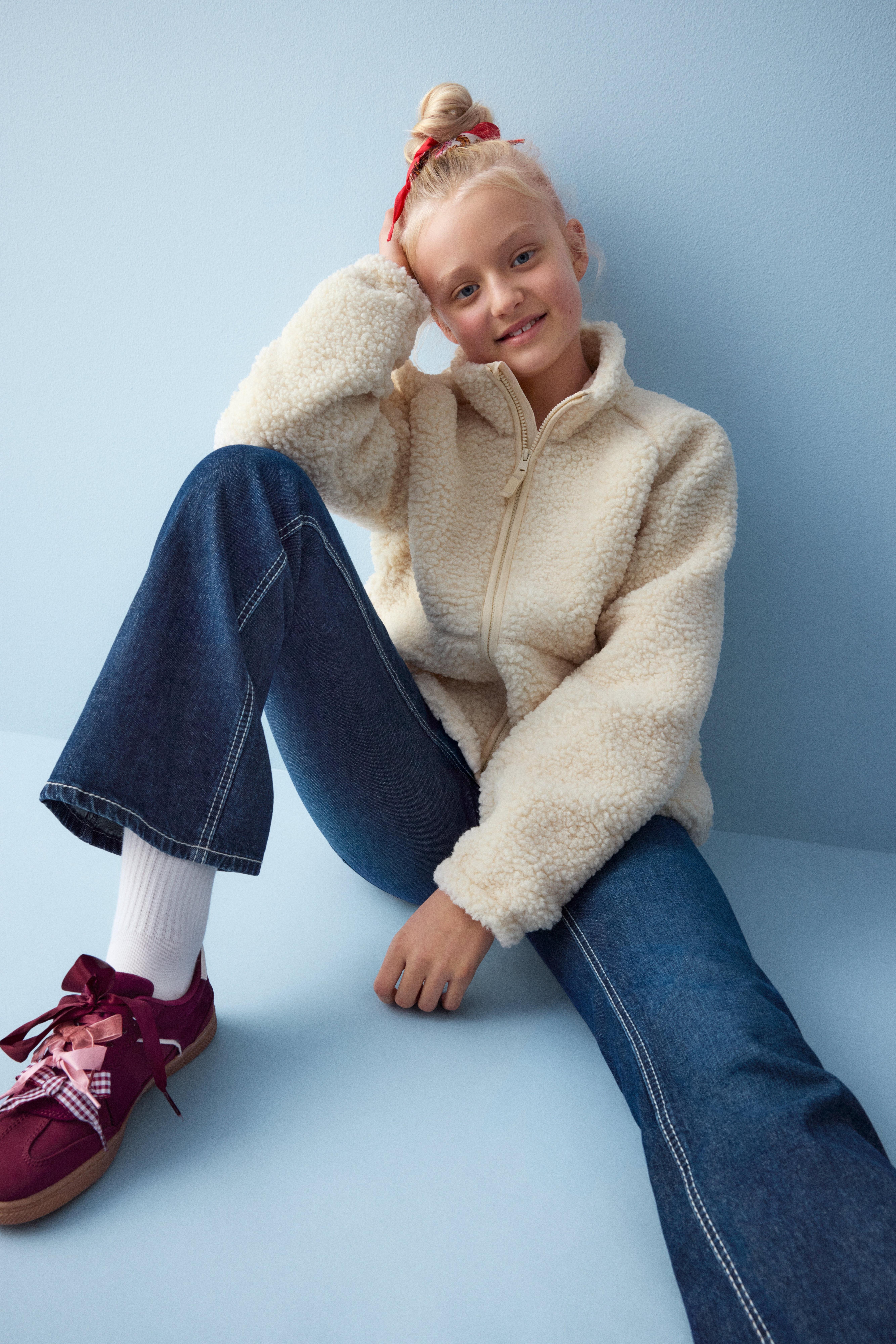 En bild på Harlow, 11 år, klädd i en beige pilejacka och jeans.