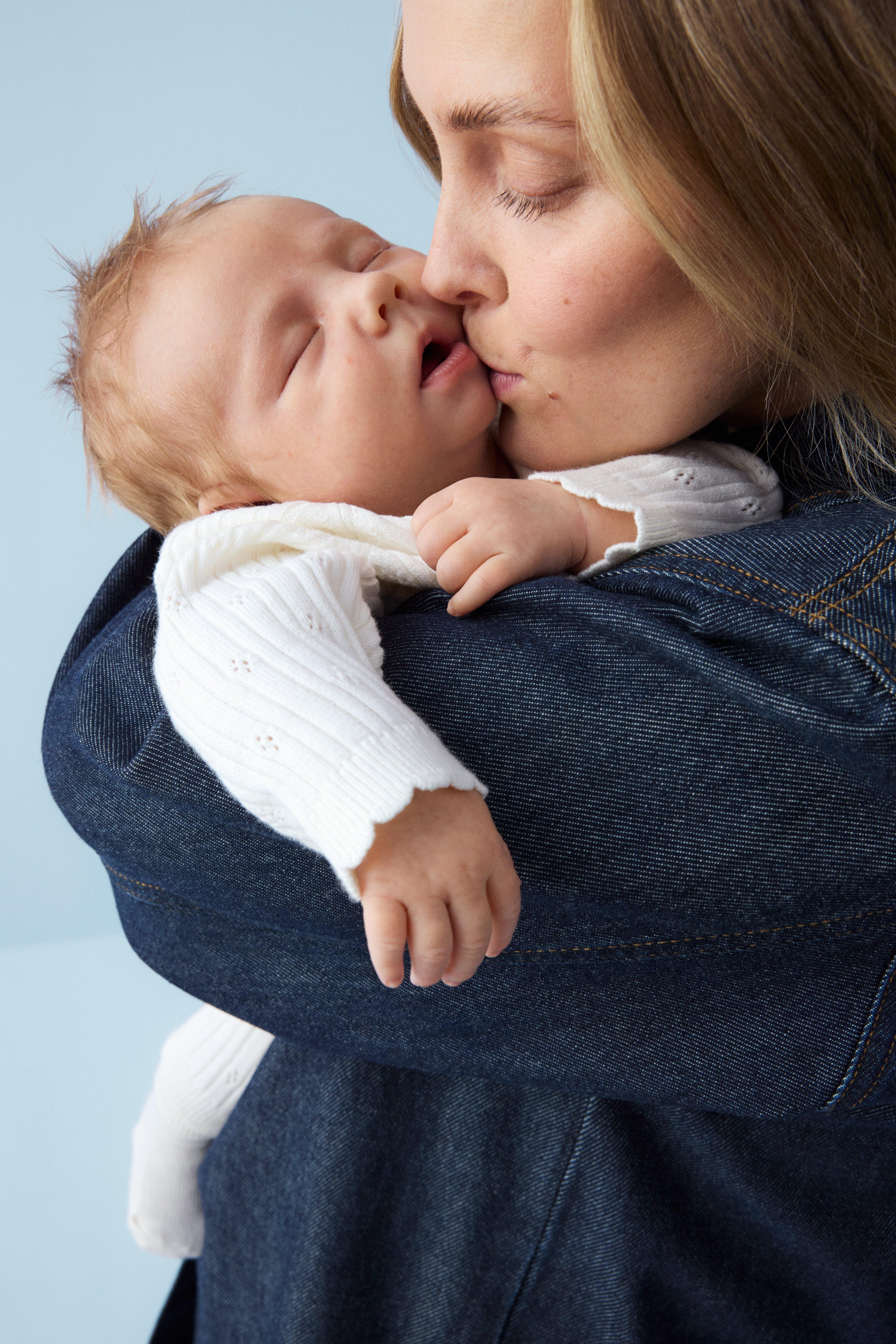 Šťastné a smejúce sa bábätko v žltých letných šatách stojí na lúke plnej kvetov.