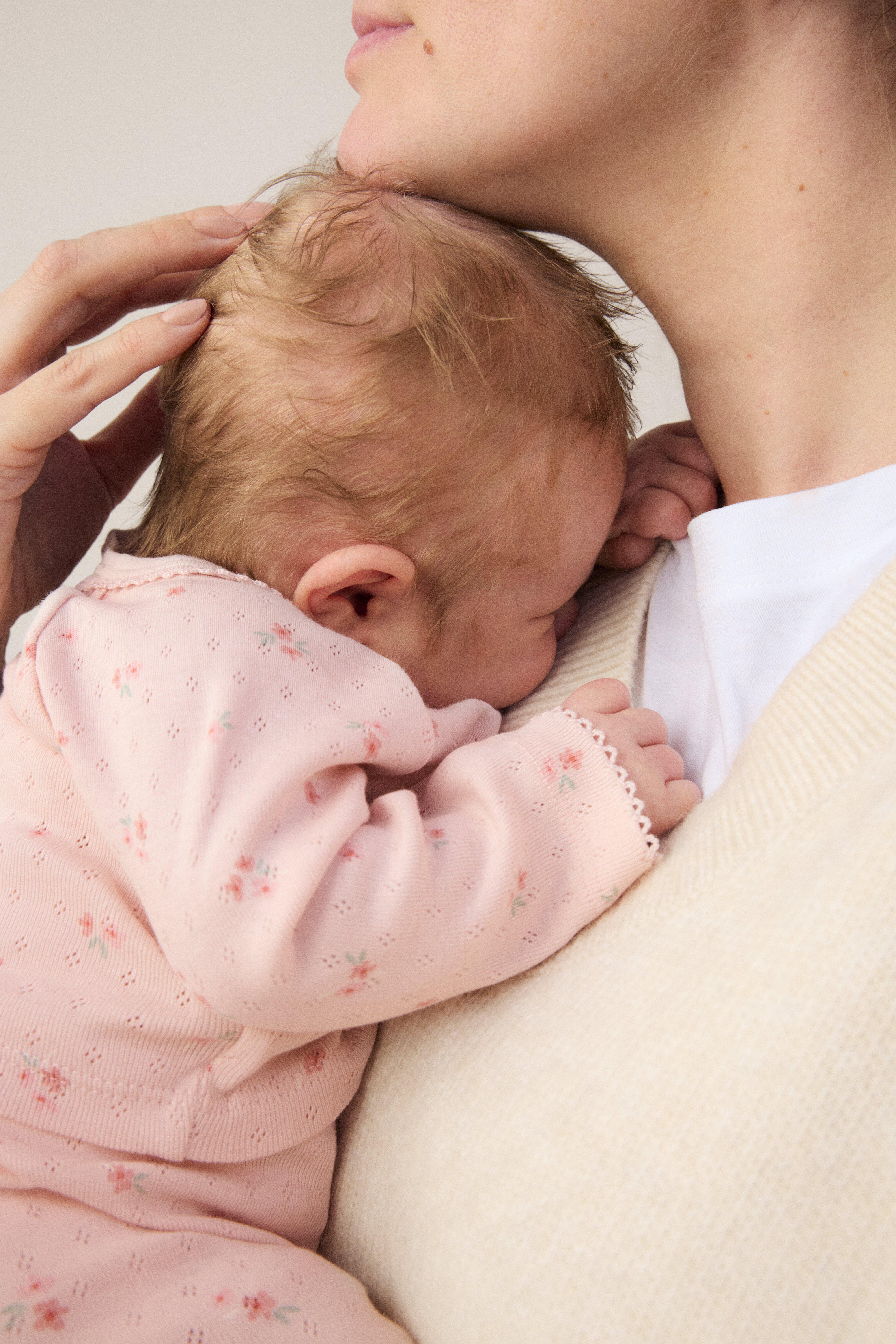Usmievajúce sa a šťastné bábätko leží na chrbte na tmavomodrej deke. Je oblečené v mäkkom a pohodlnom štartovacom sete od Lindex.
