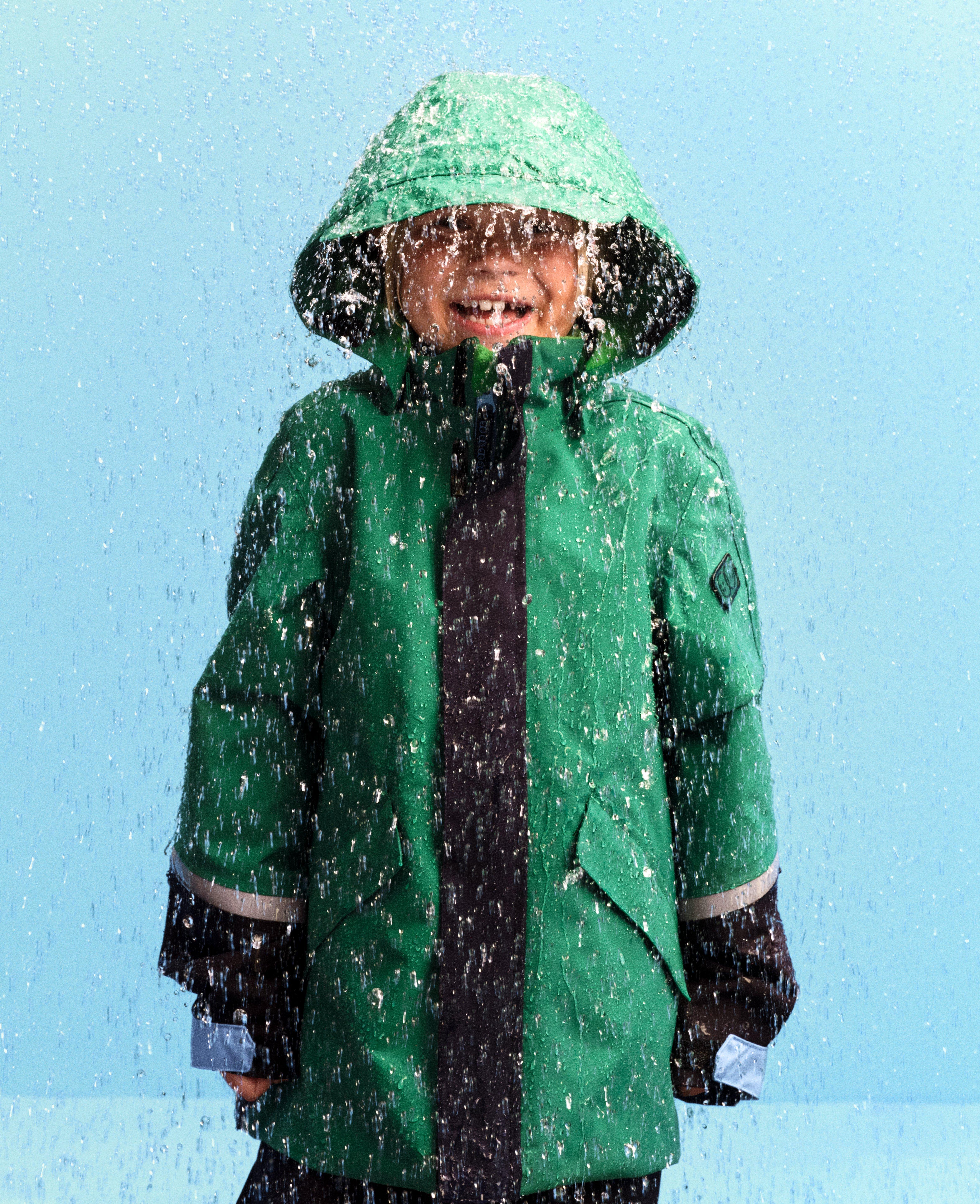 Ett barn i regnet i en grön Lindex skaljacka