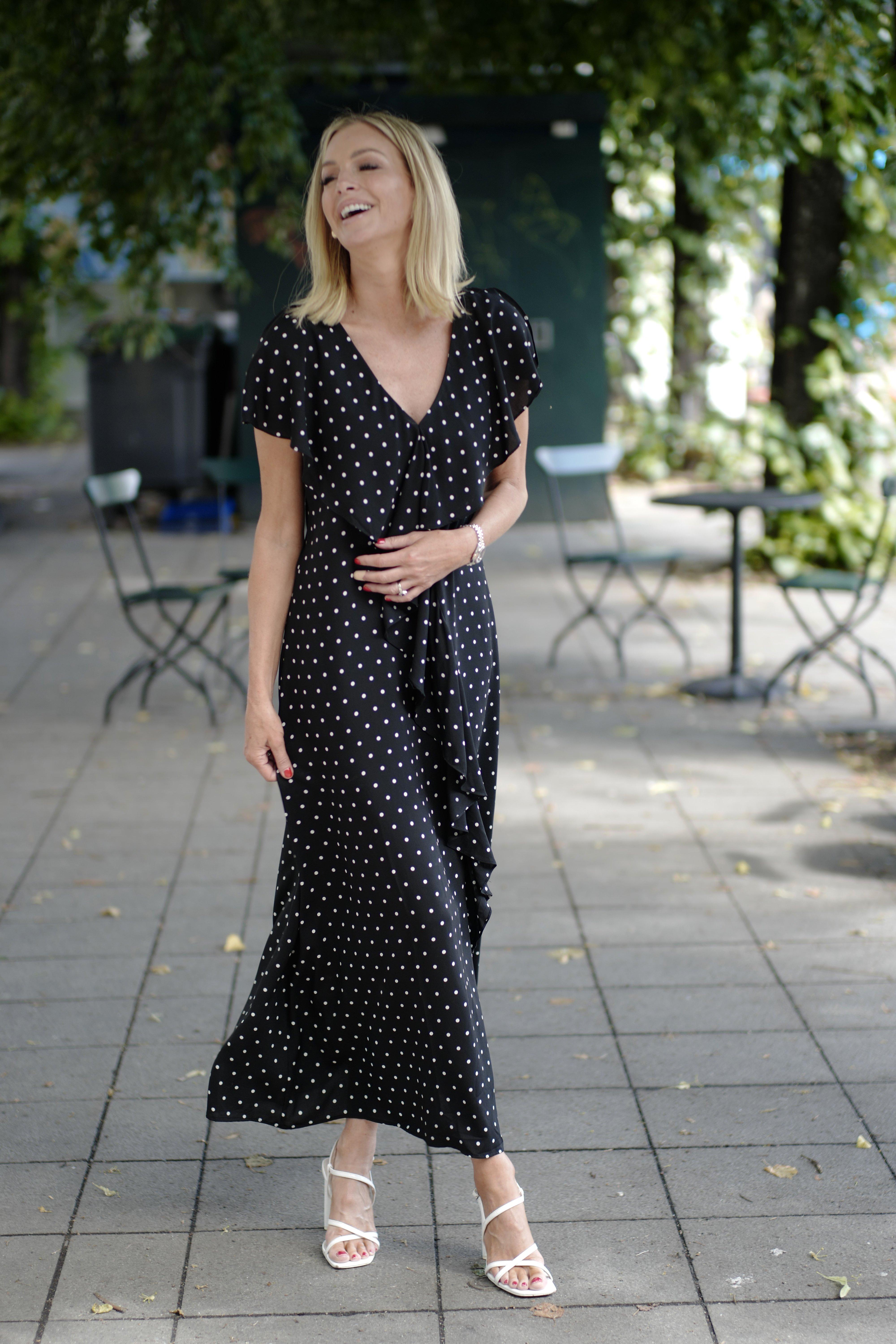   Kathrine, klädd i en svart långklänning med vita prickar och kort ärm. Kathrine, dressed in a long black dress with white polka dots and short sleeves.