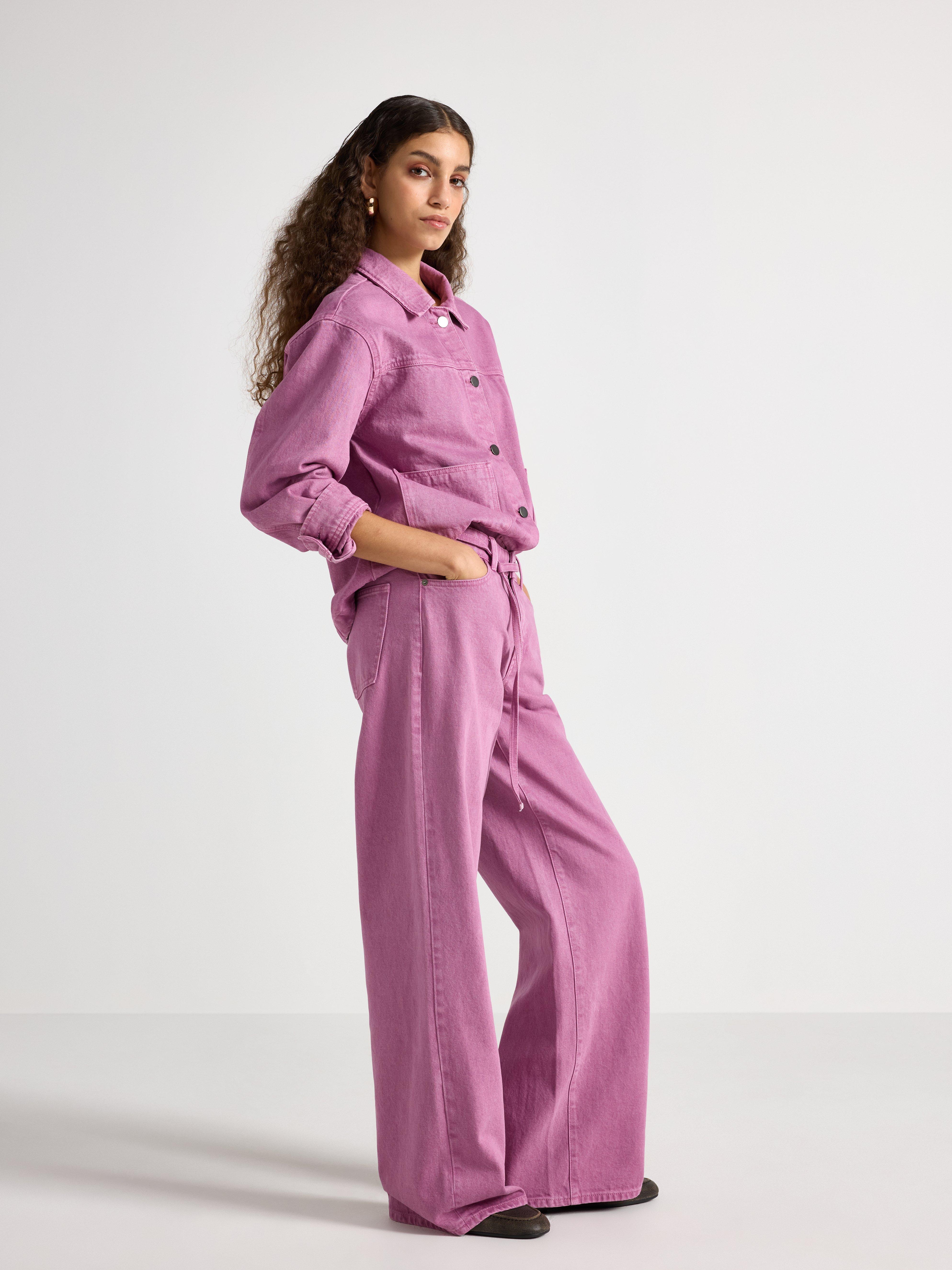 A woman photographed from the side wearing a purple shirt and pants.