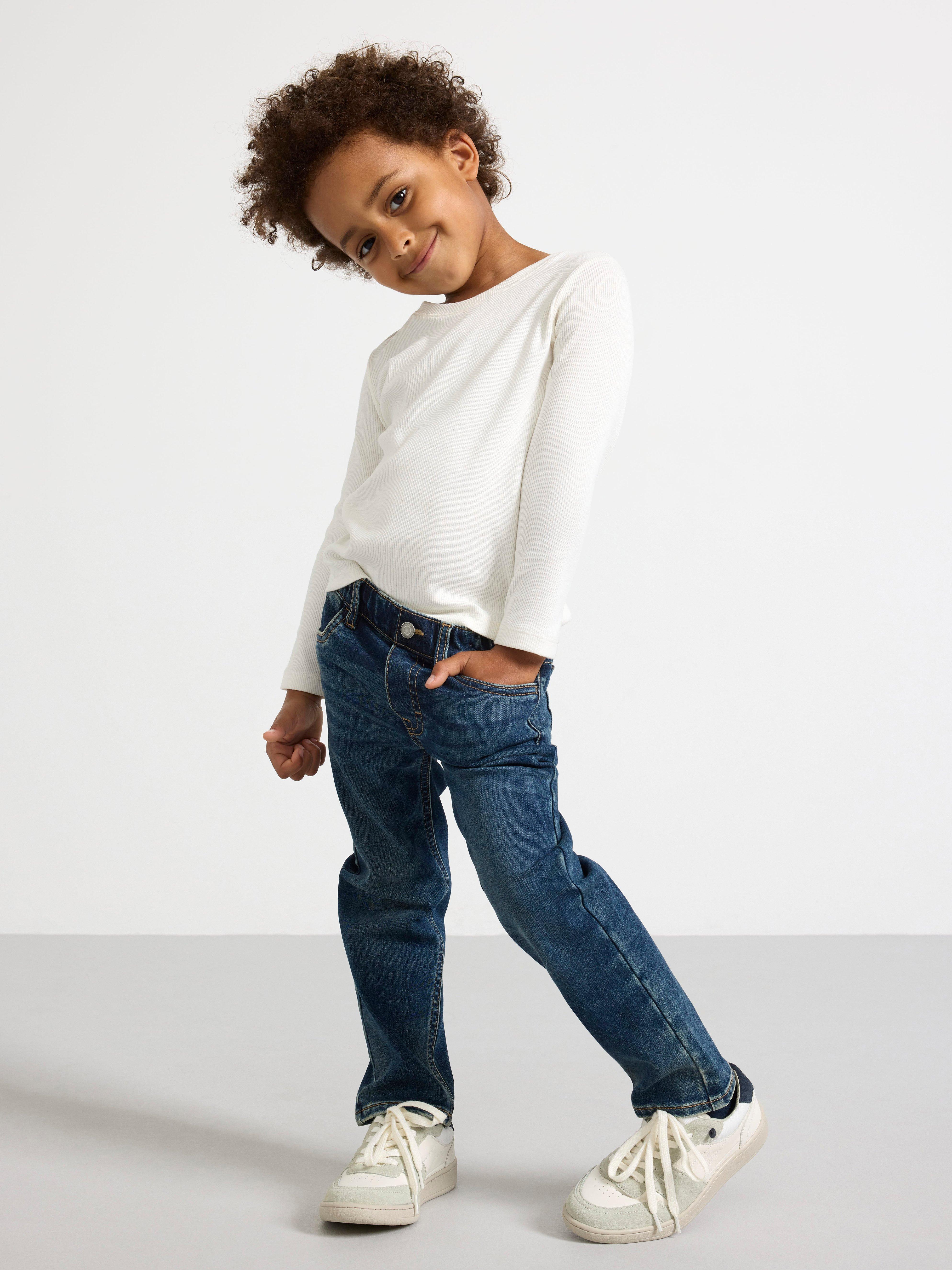 A young child wearing a white sweater and a pair of blue Staffan jeans.