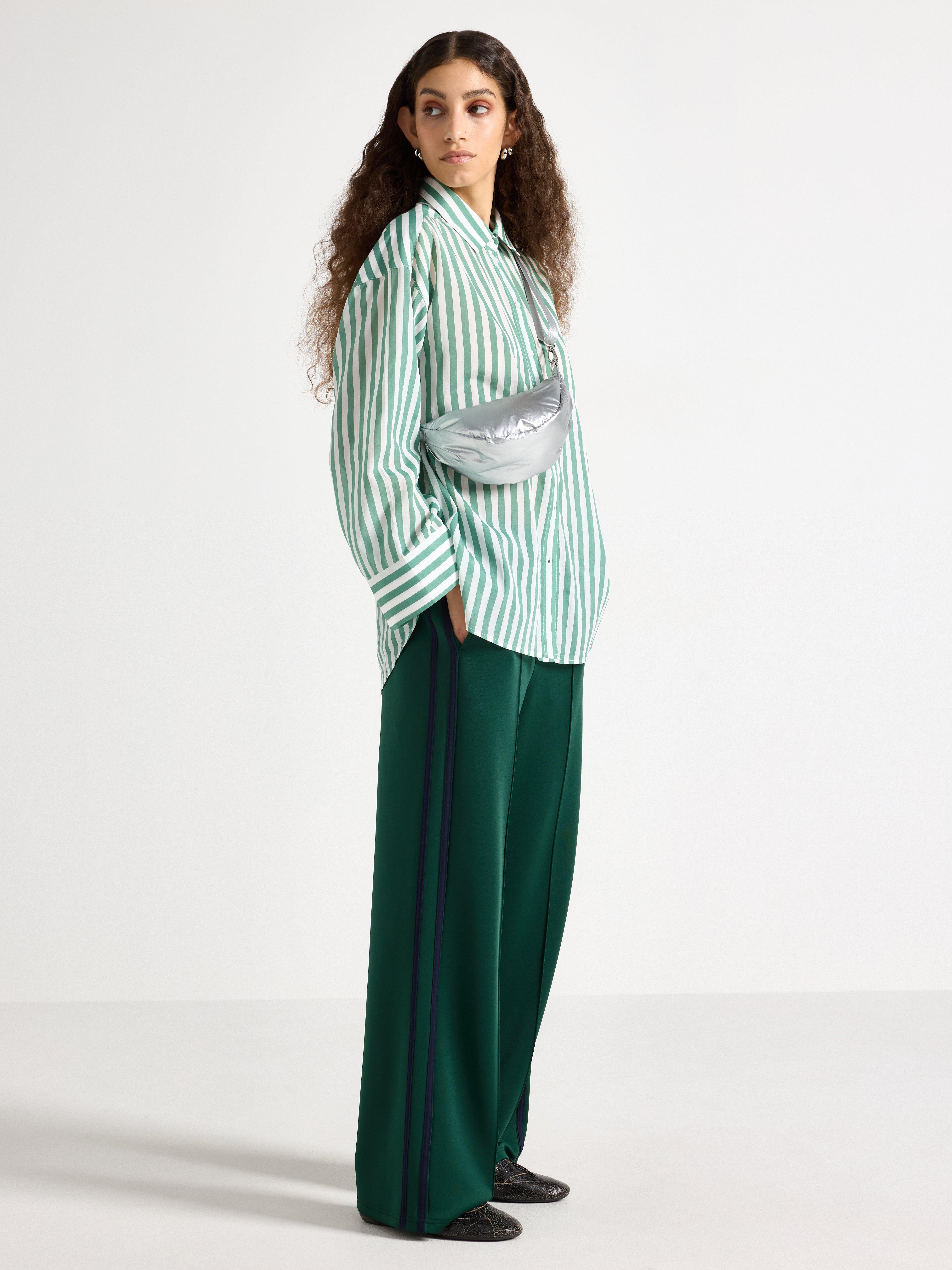  A woman wearing a white and green striped shirt and a pair of green trousers.