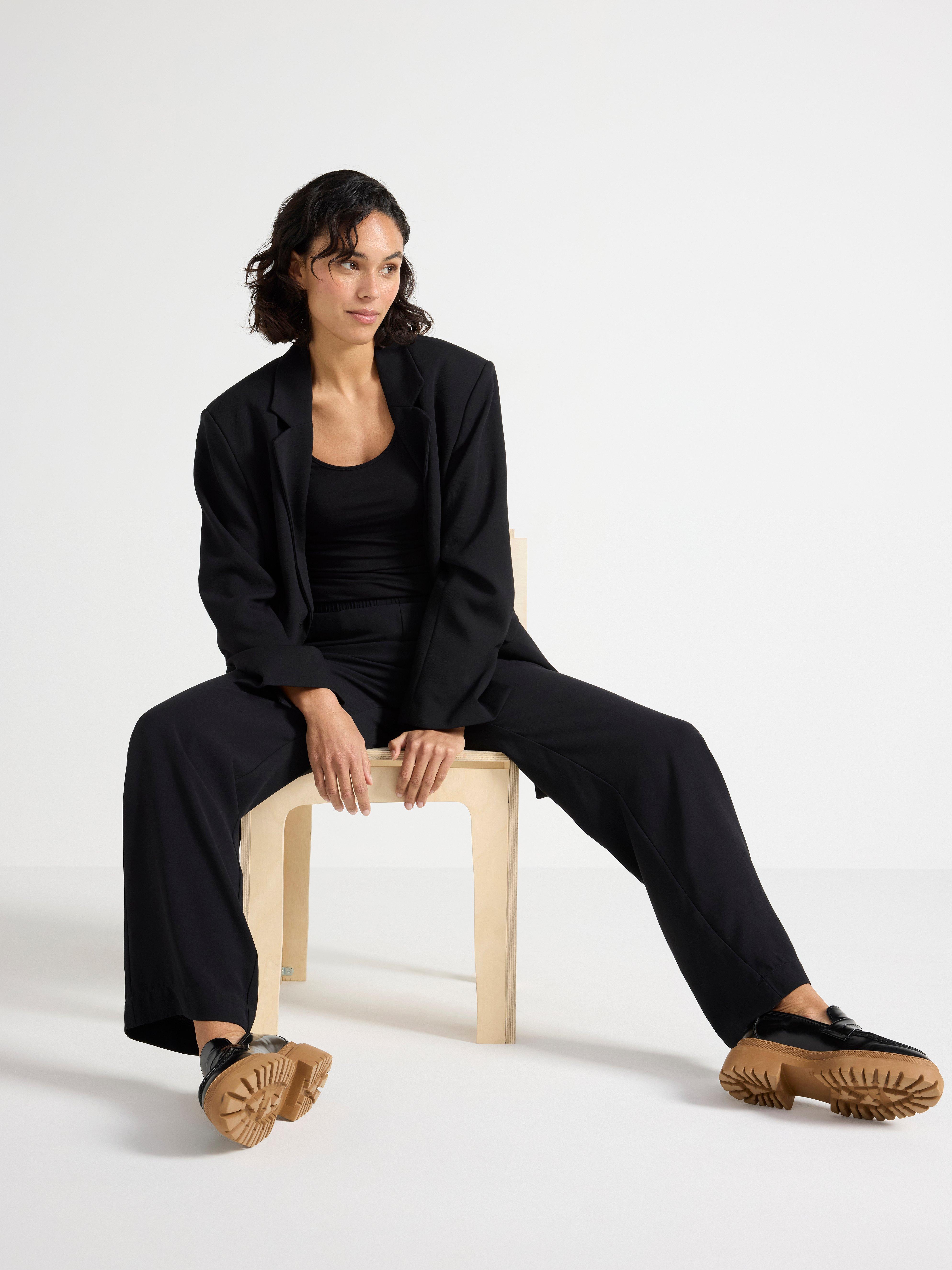 A woman dressed entirely in black sits on a wooden stool.