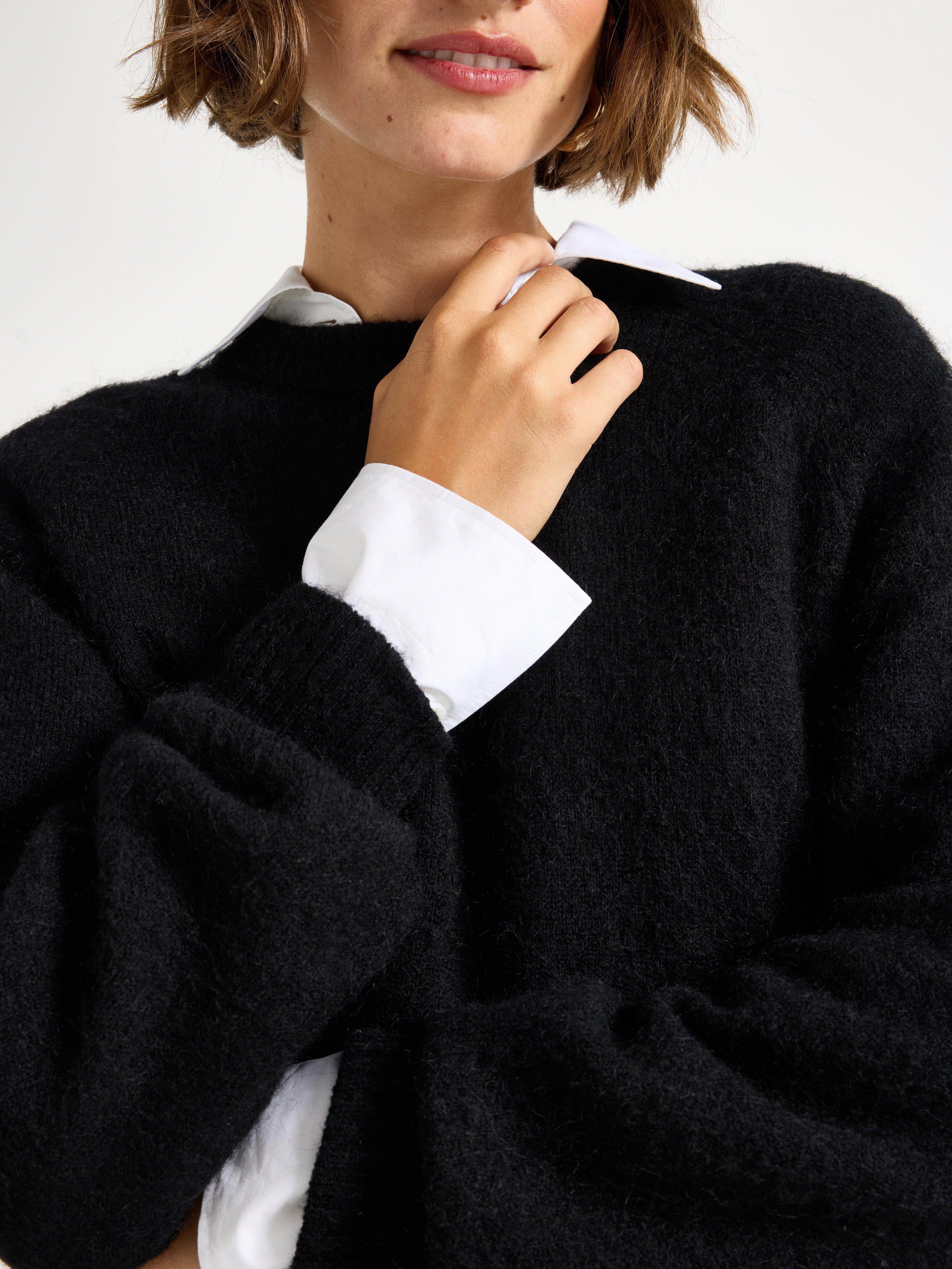 Close-up of a woman in a black sweater, under the sweater she has a white shirt.