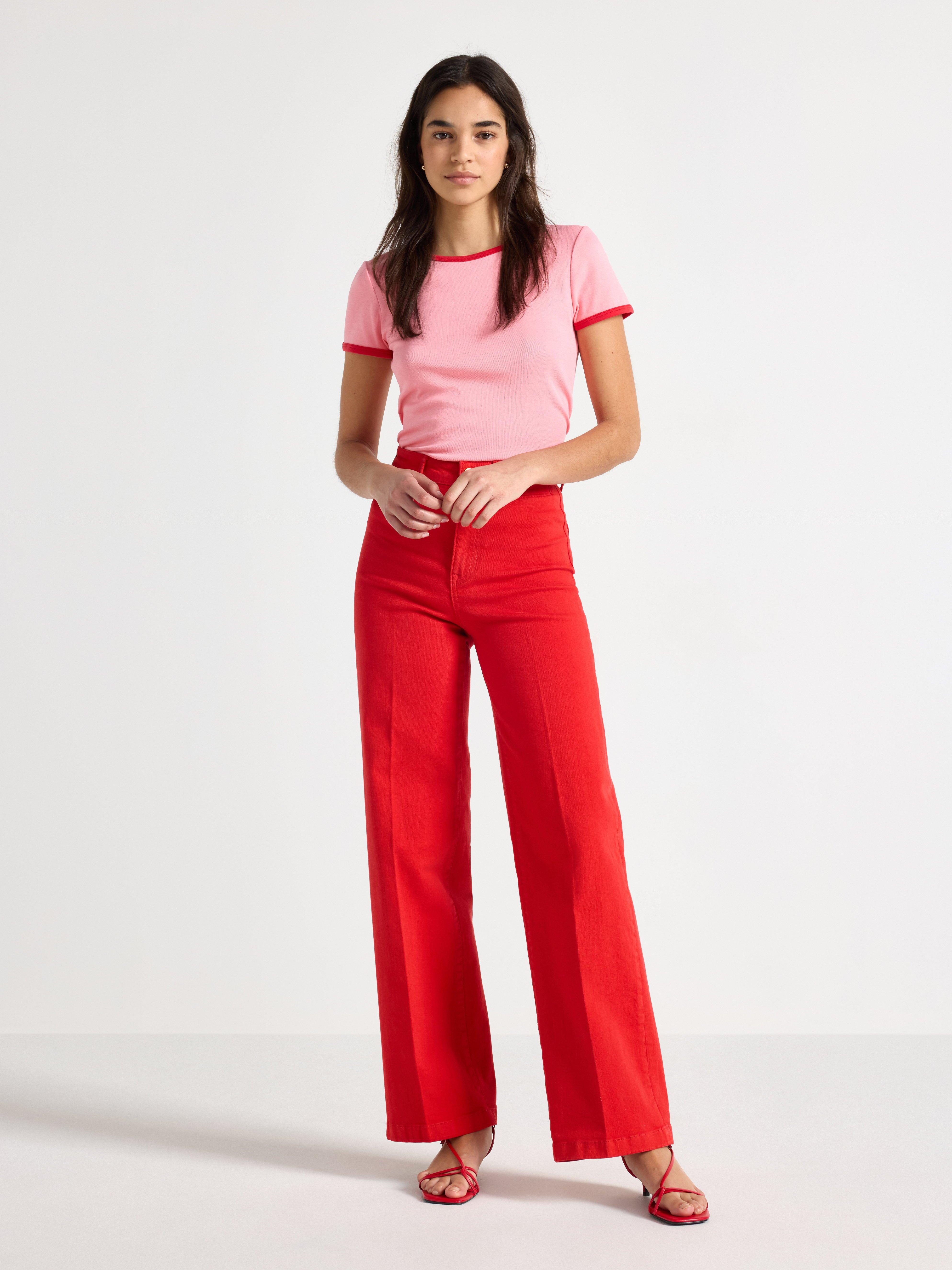 En kvinna i ett par röda byxor och en rosa kortärmad topp med röda kanter.