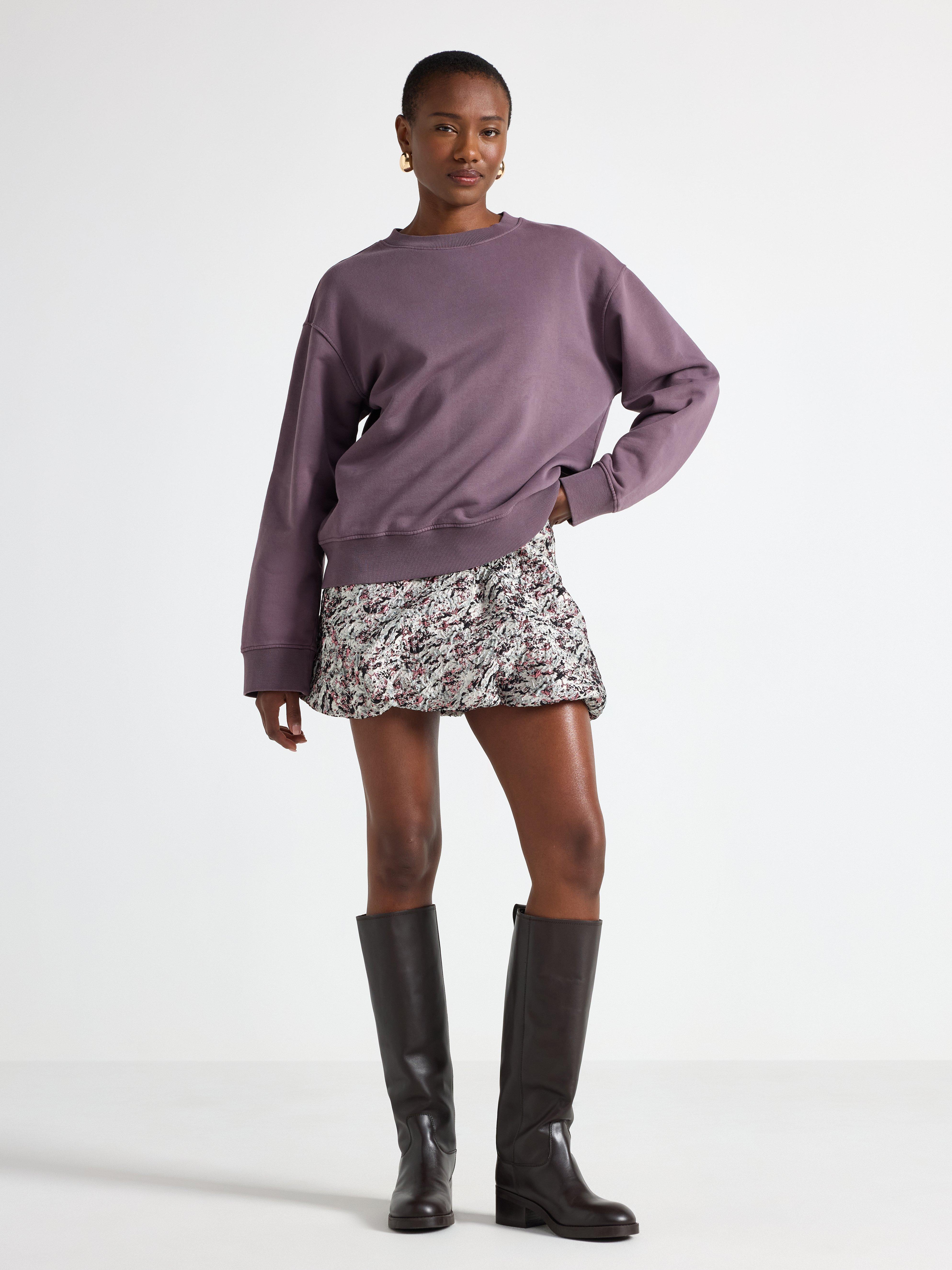 En kvinne som har på seg en lilla genser og et kort svart-hvitt mønstret skjørt.