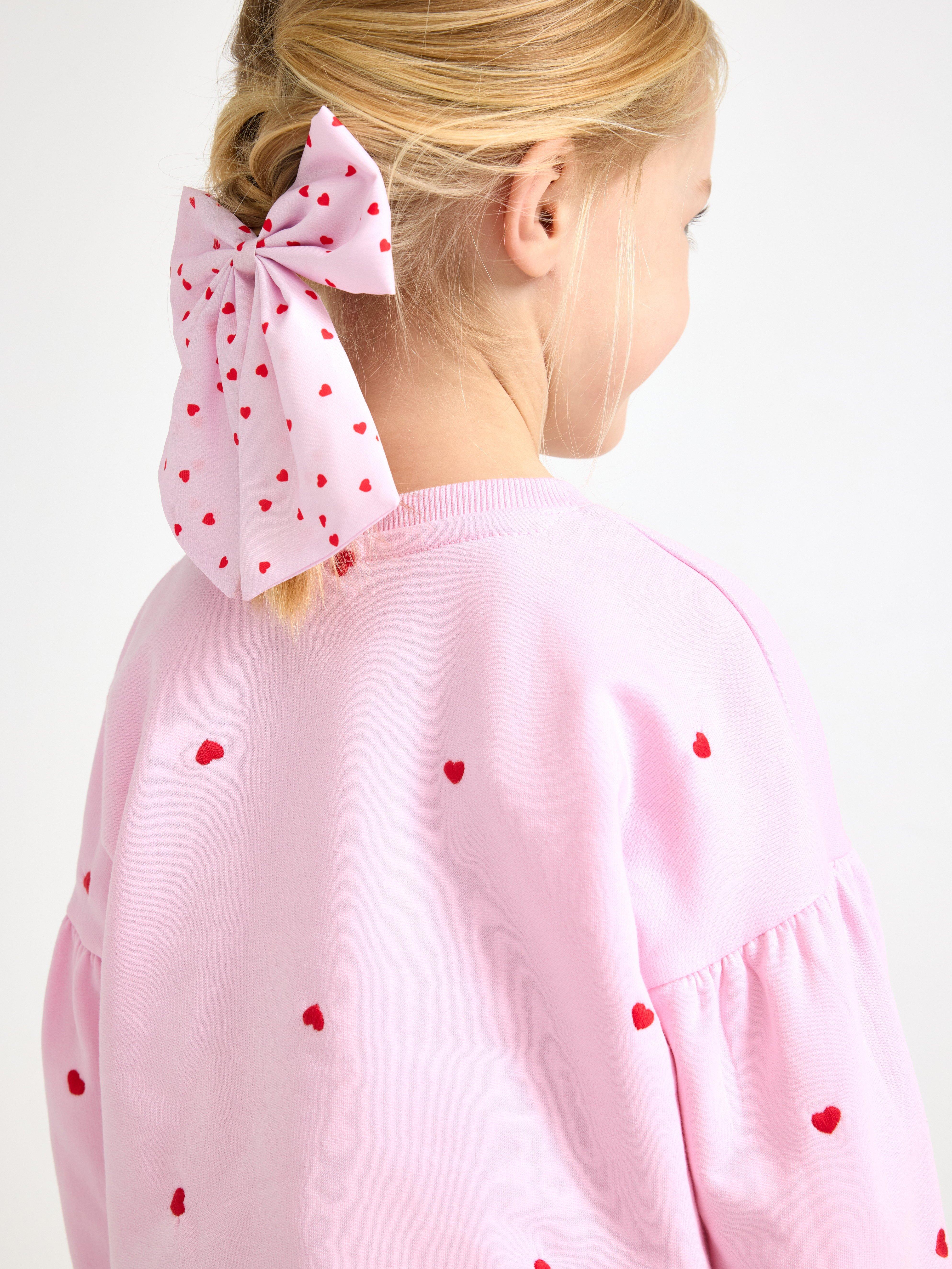 Close-up of a girl with a pink bow with hearts in her hair.