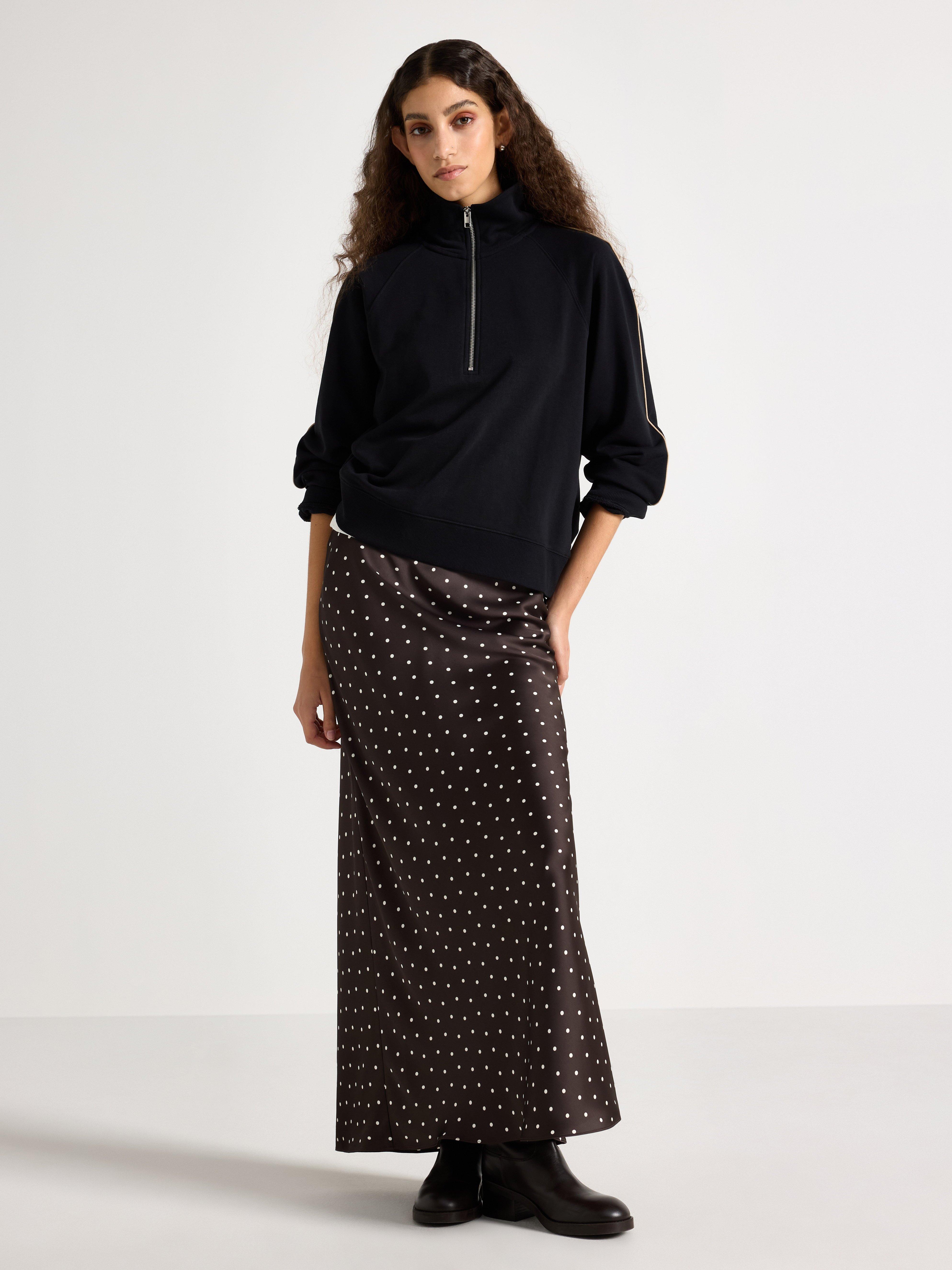 A woman wearing a black sweatshirt with half-zip and a skirt with white dots.