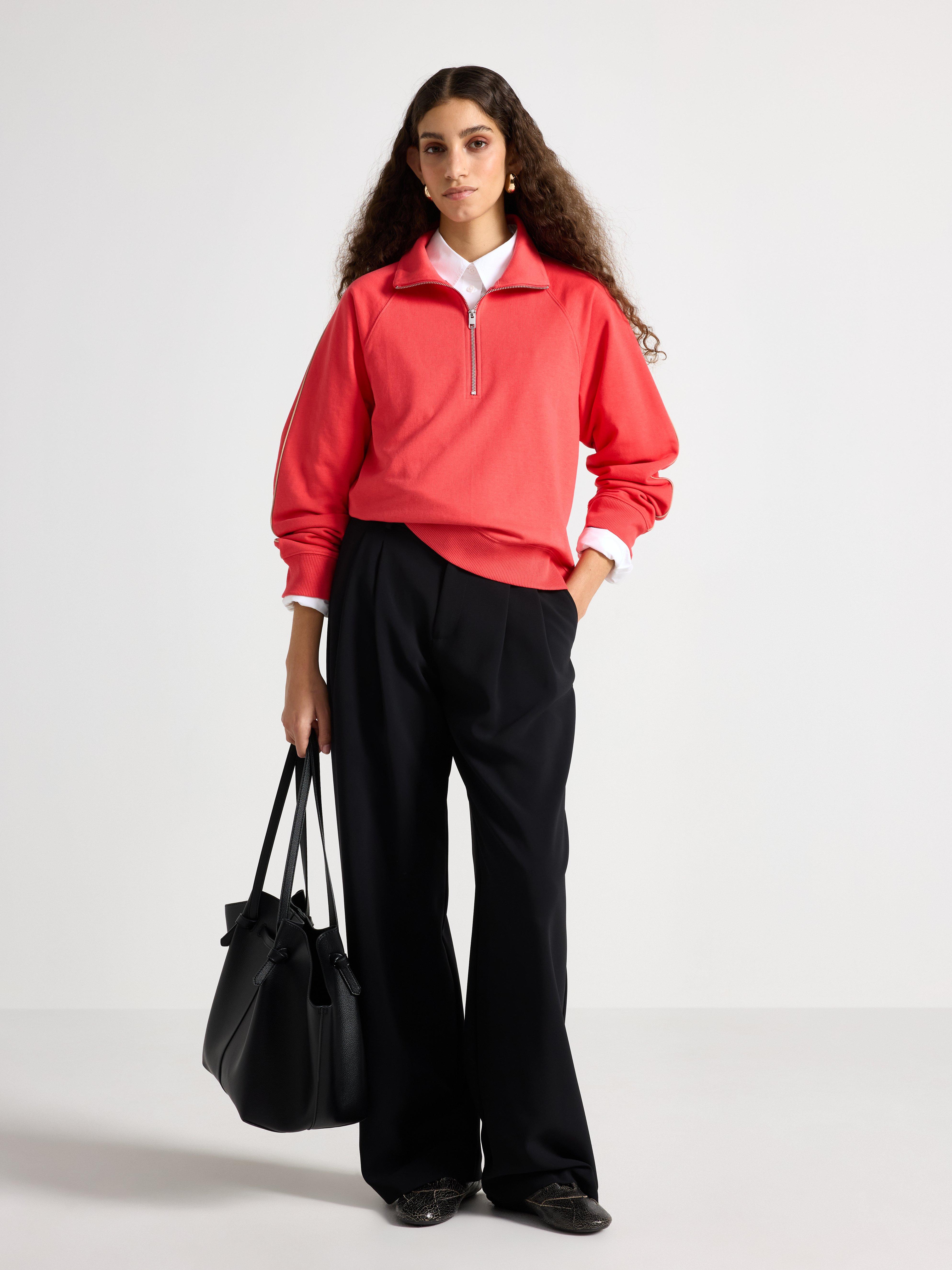 En kvinna som bär en mörk korallfärgad tröja med halvdragkedja.