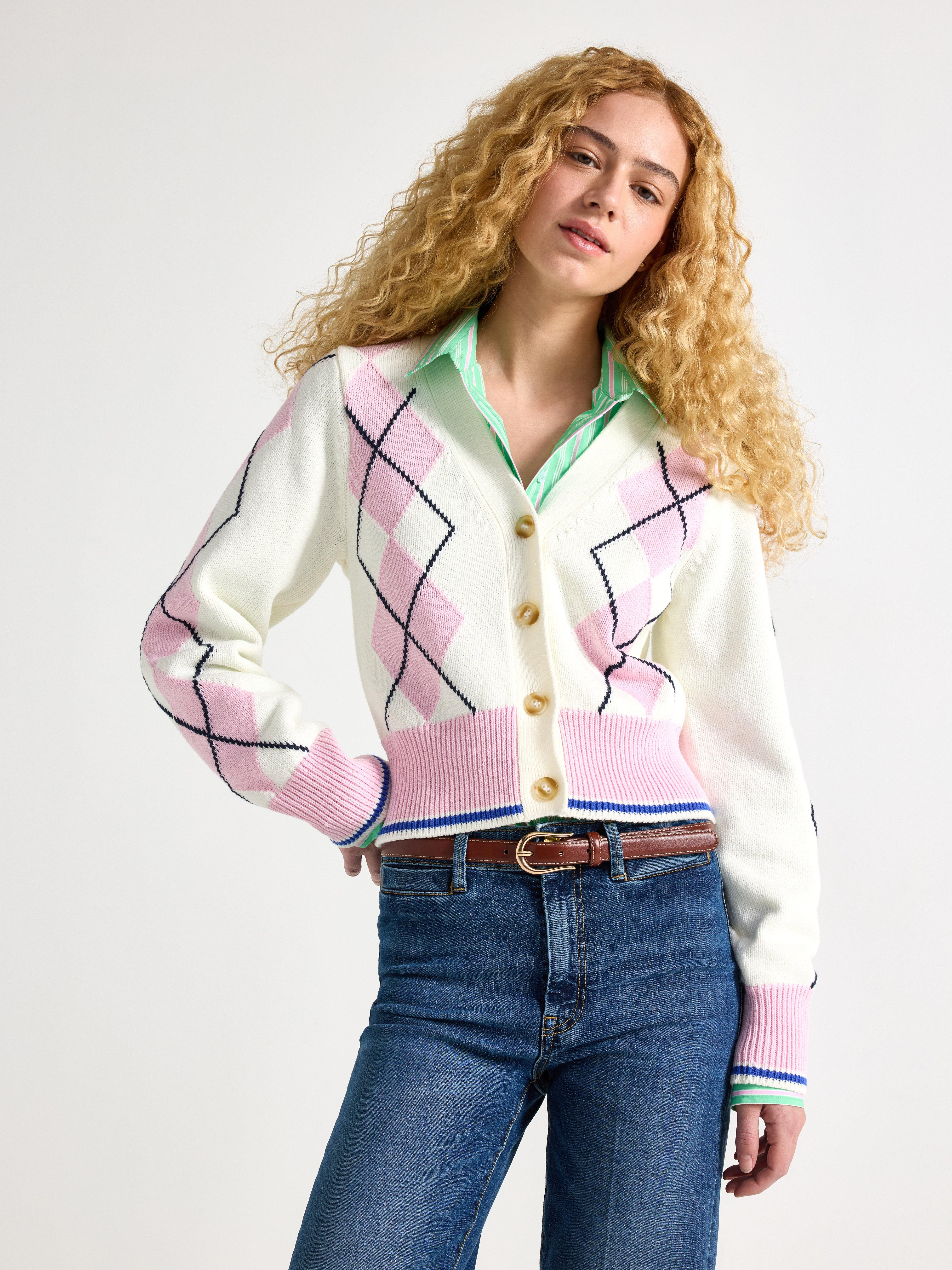 Detailní záběr ženy v kardiganu s kosočtverečným vzorem v bílé a růžové barvě s pod ním světle zelenou košilí.