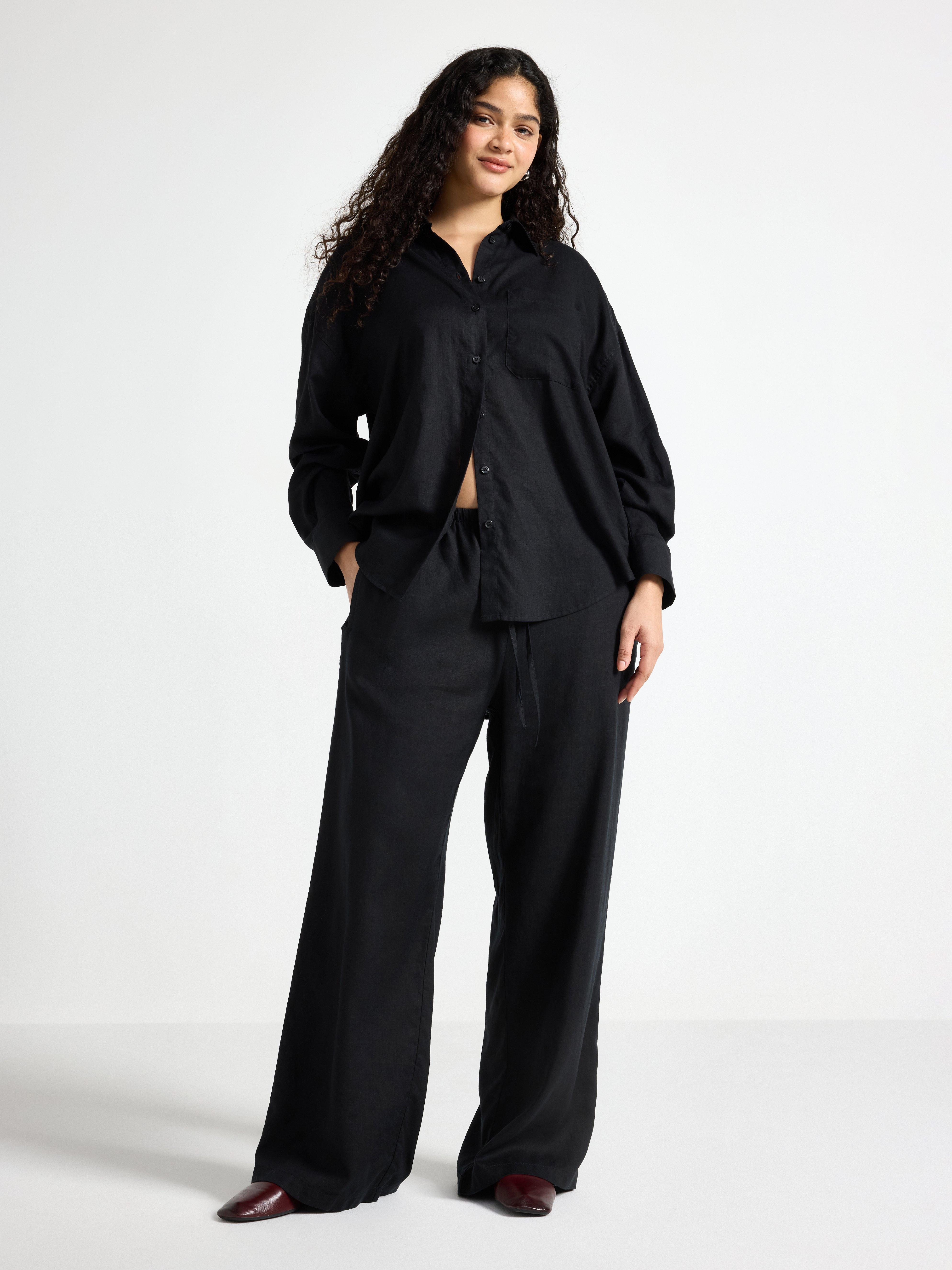 A woman dressed entirely in black stands against a gray background.