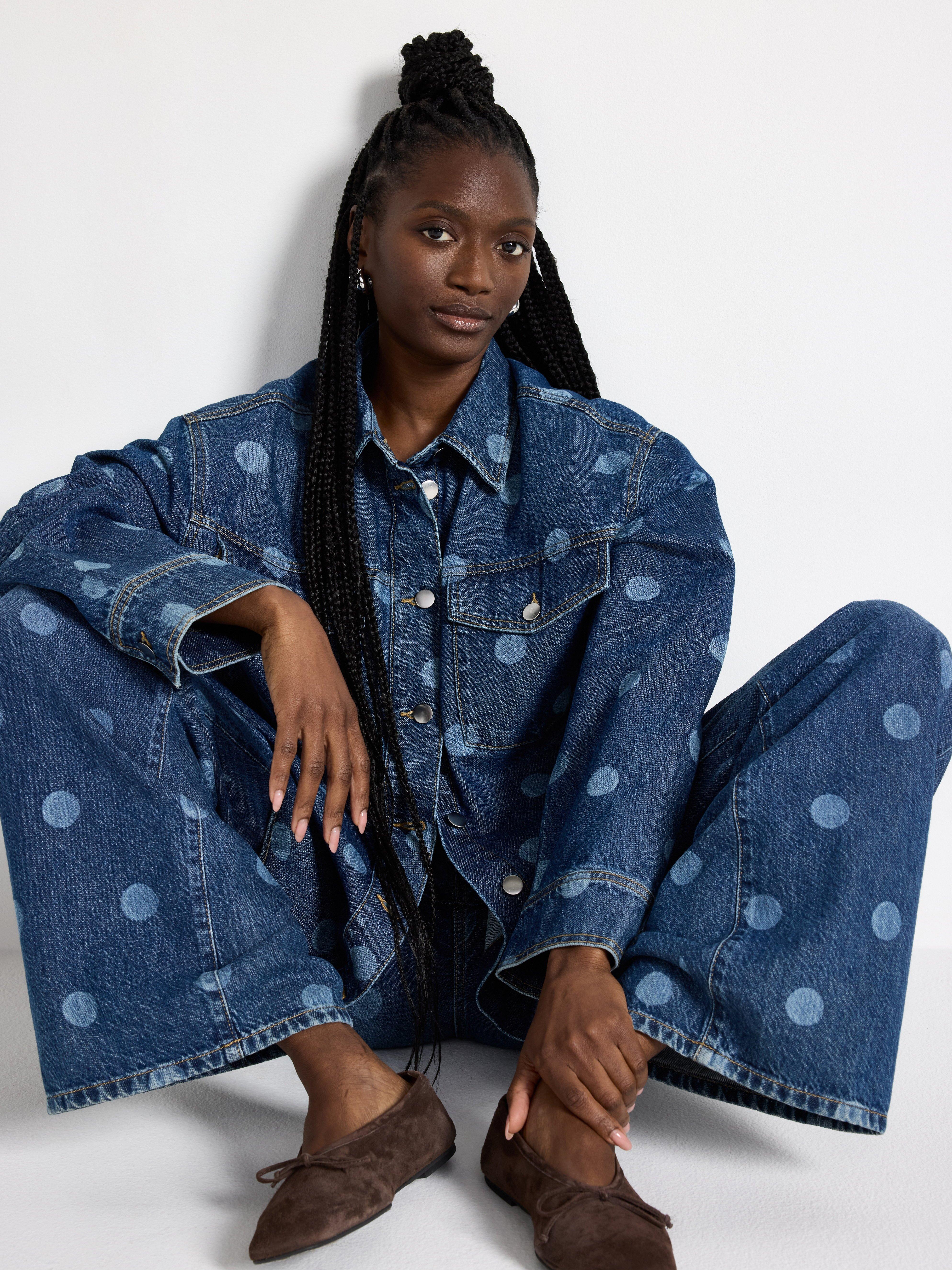 A seated woman wearing a denim shirt and jeans with a polka dot pattern all over the garment.