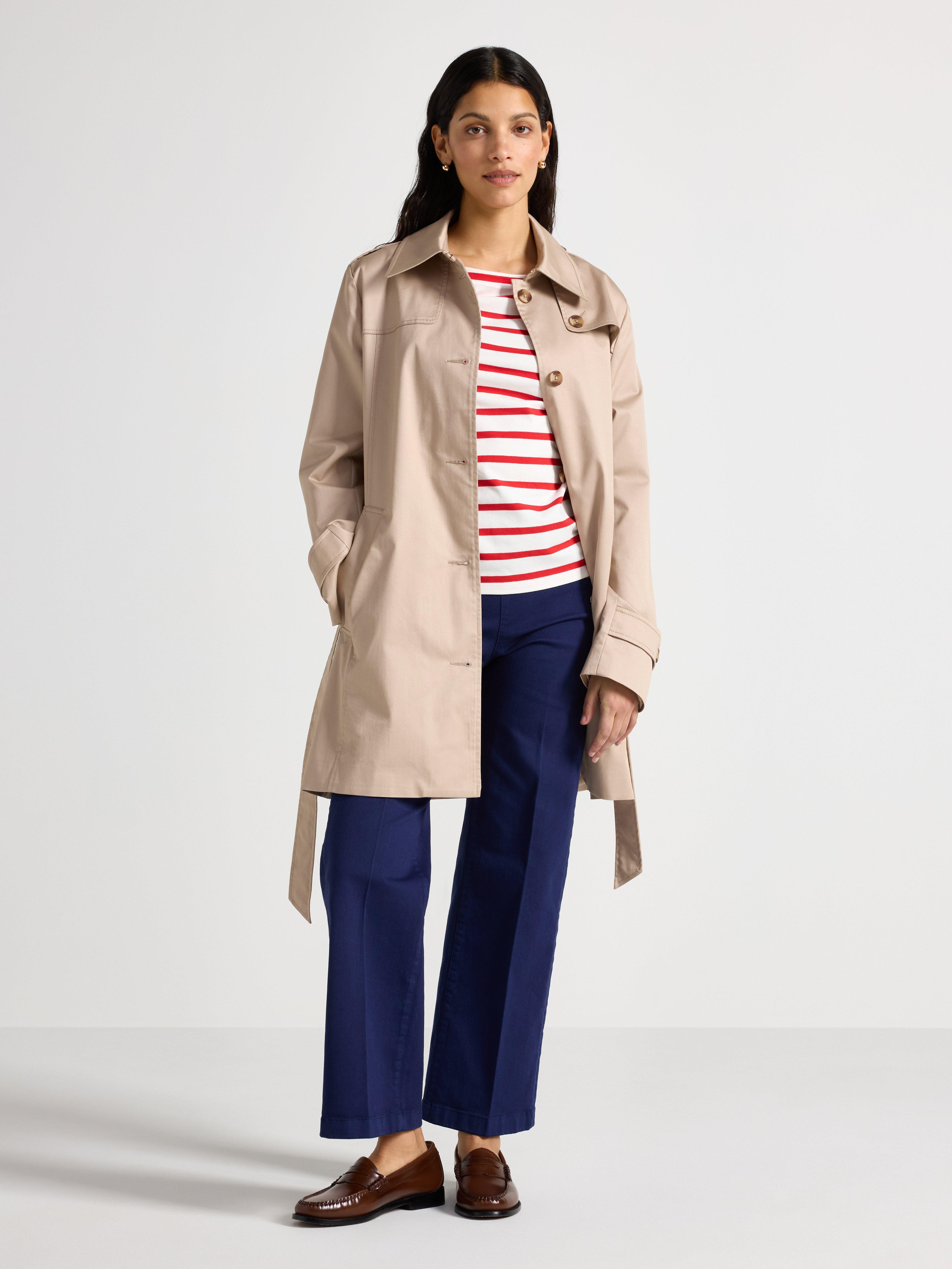  A woman in a red and white striped sweater, beige coat and dark blue pants.