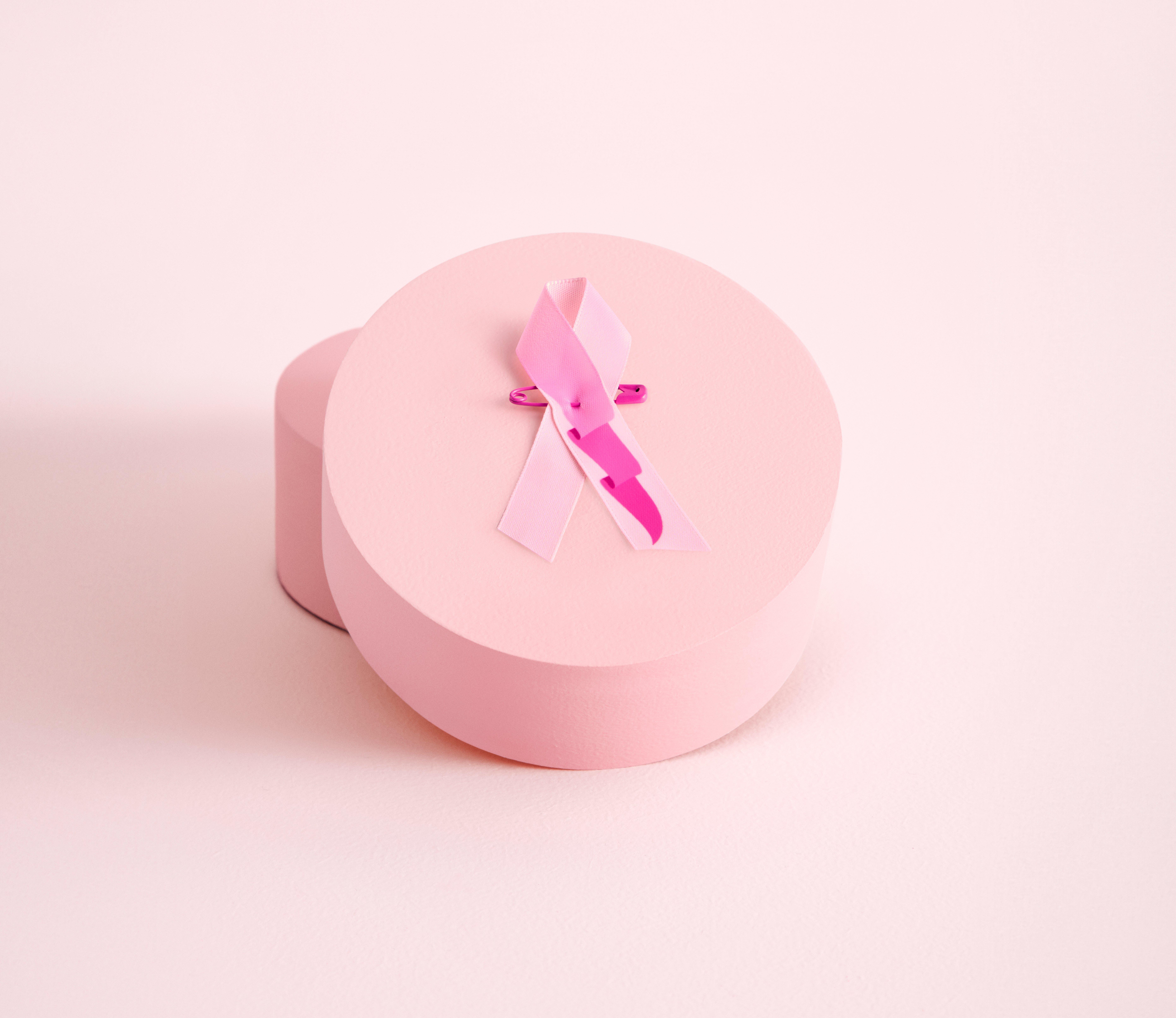 Tämän vuoden Roosa nauha lähikuvassa, joka lepää pyöreän vaaleanpunaisen laatikon päällä. Nauha on vaaleanpunainen ja siinä on kuvio, jossa viiri liehuu tuulessa.