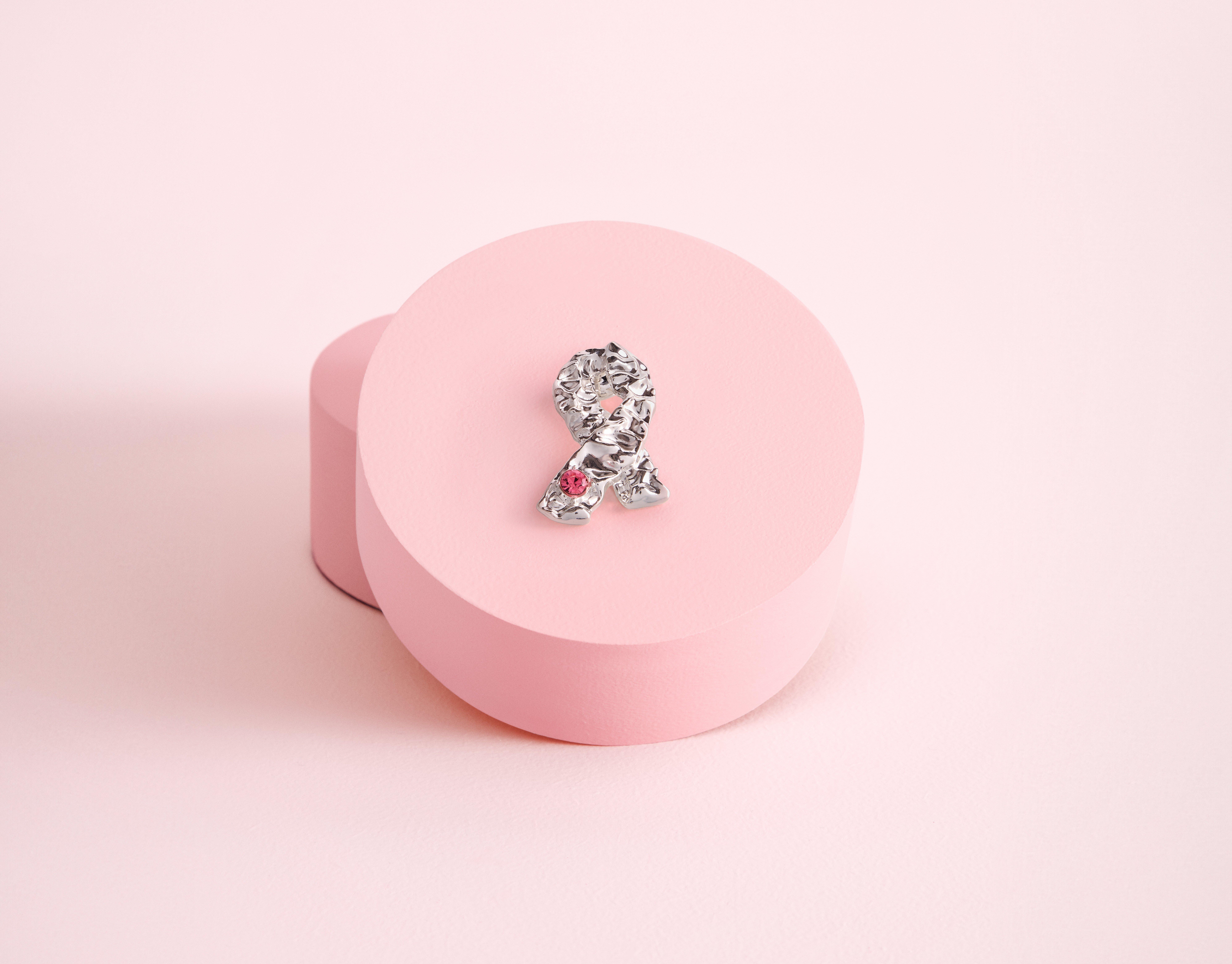 Et nærbilde av årets rosa sløyfebrosje som ligger oppå en rund rosa eske.