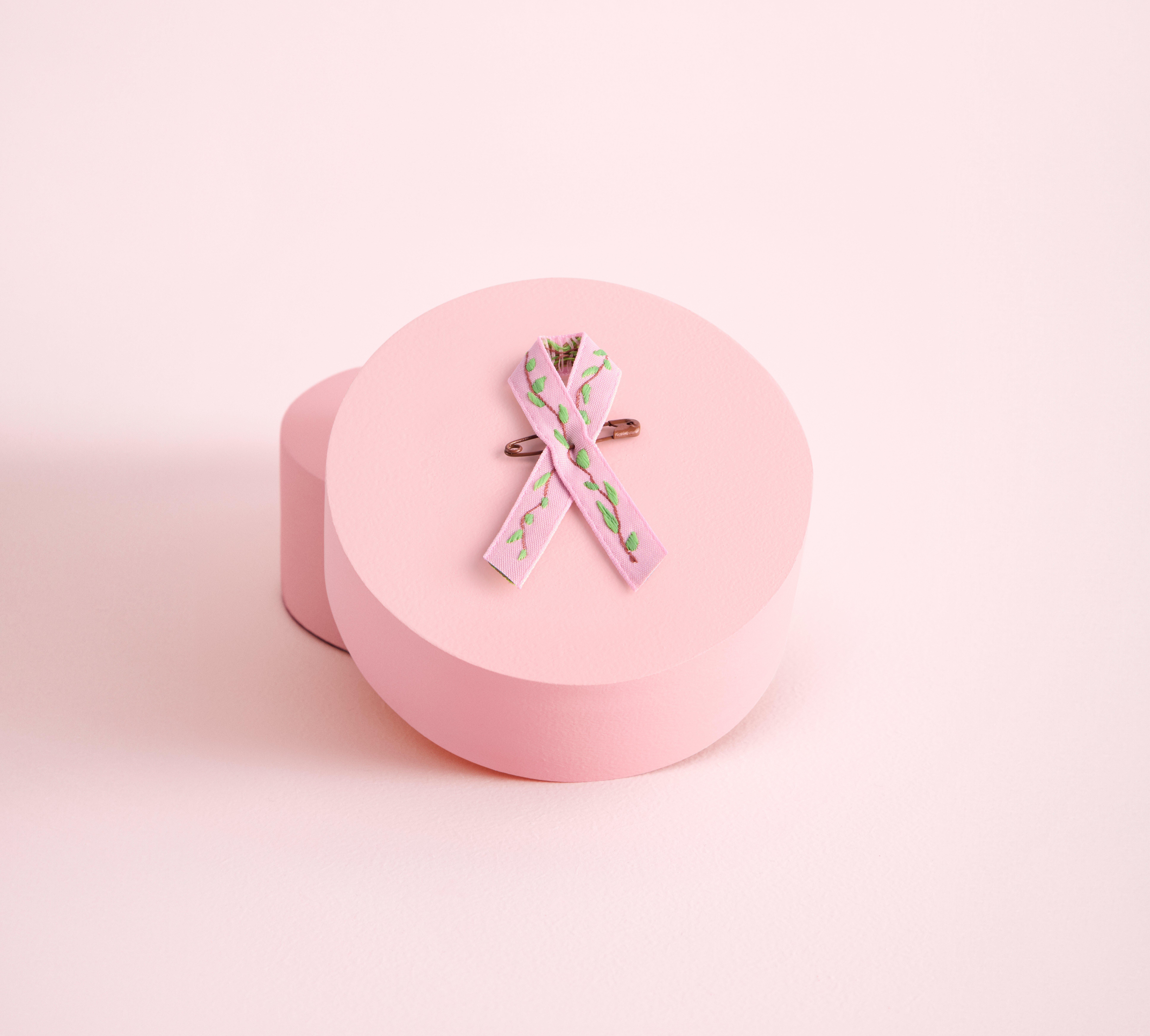 En närbild på årets rosa band som ligger ovanpå en rund rosa ask. Bandet är ljust rosa och och har ett mönster av ljust gröna löv på en kvist.