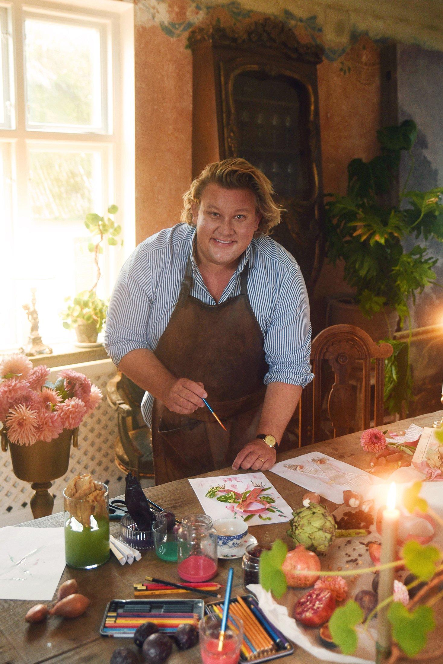 Årets designer Karl Fredrik Gustafsson står vid ett bord och målar.
