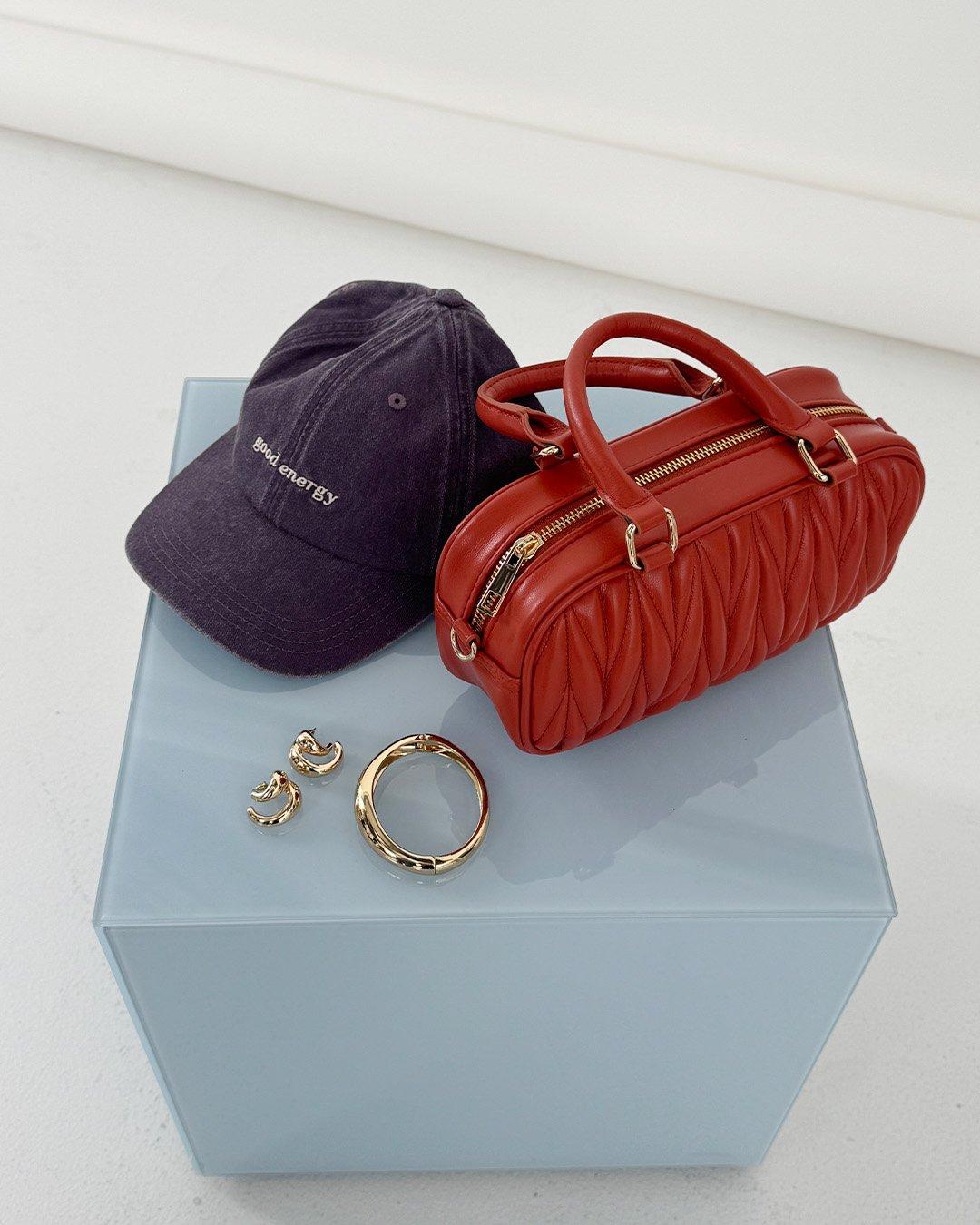 Detailní záběr na tašku, čepici a nějaké šperky.