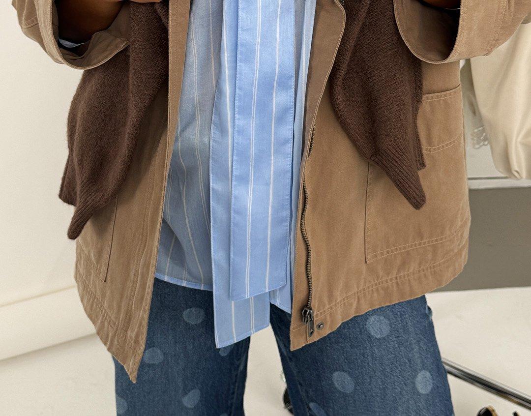 Detailní záběr ženy oblečené v modrých džínách s puntíky, modrém pruhovaném tričku a hnědém saku.