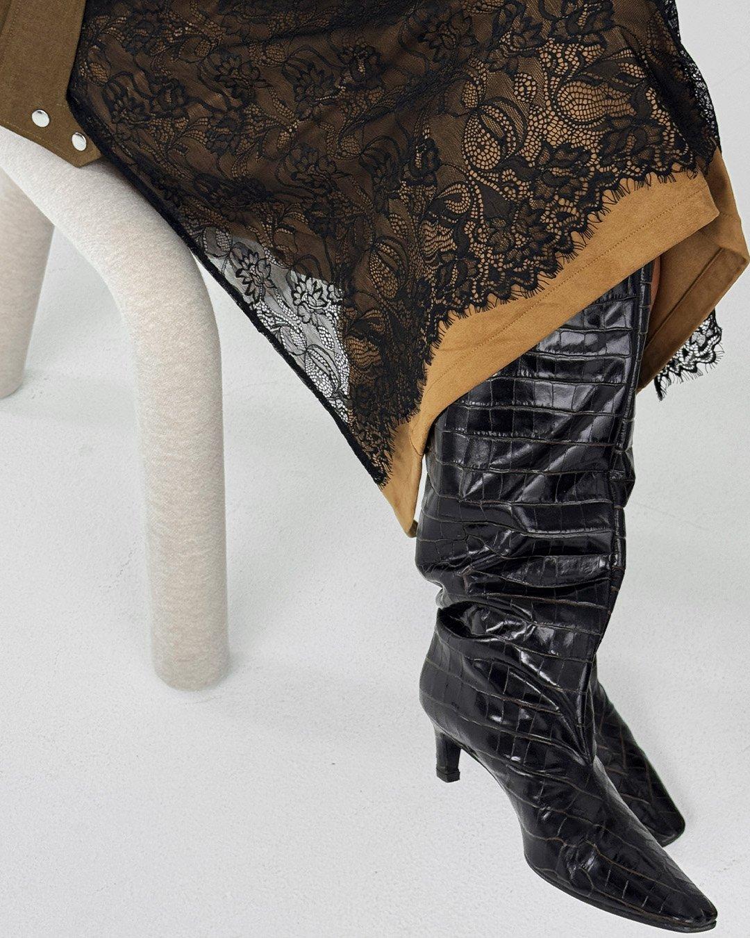 Detail černé zástěrové sukně z krajky přes hnědou sukni.