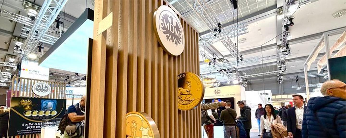 MDM-Messestand auf der World Money Fair mit Goldmünzen-Displays und Besuchern in der Messehalle
