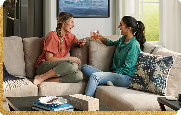 Two women sitting on a couch chatting and having wine.